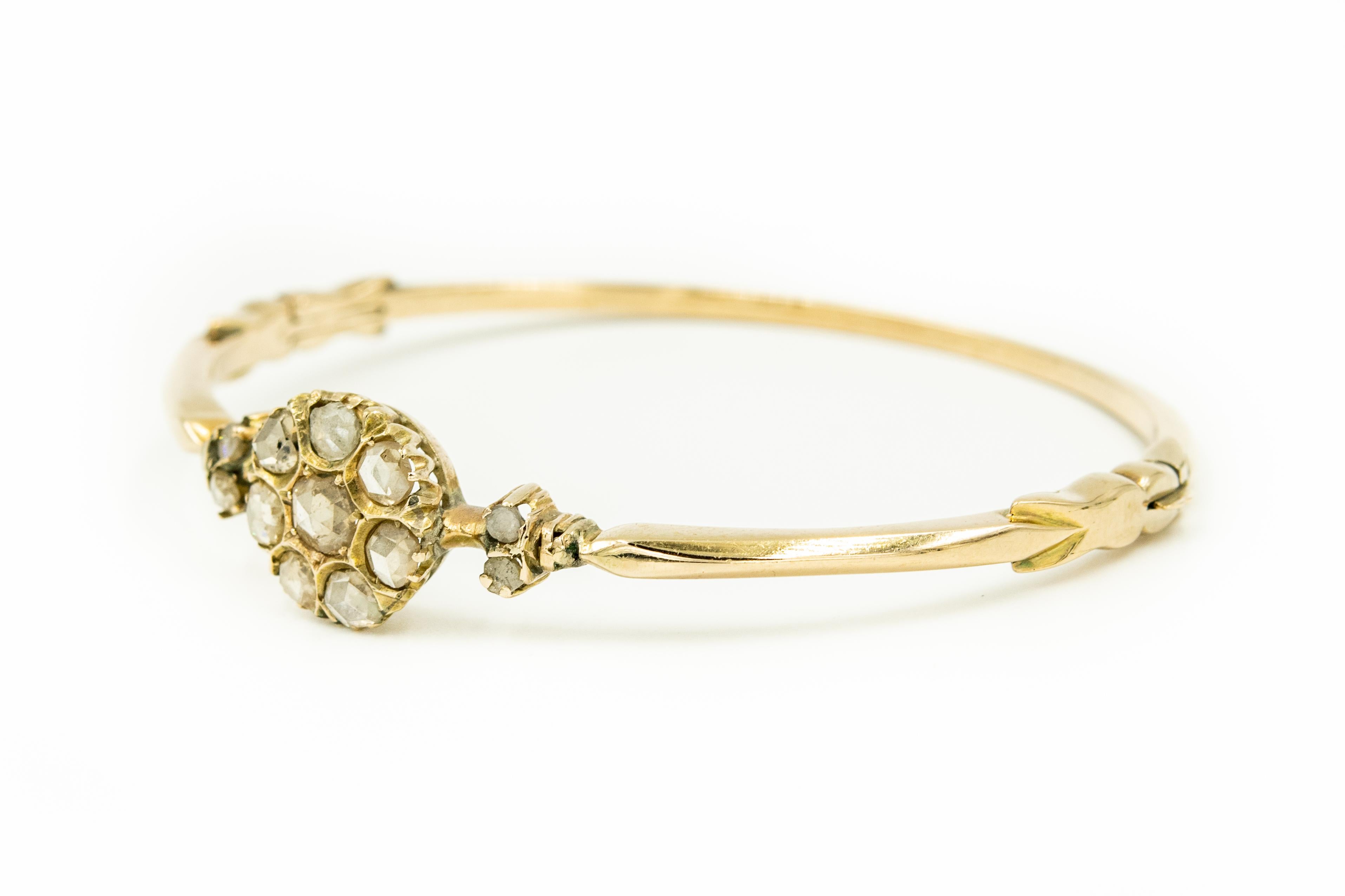 Antique Victorian 10k yellow gold bangle bracelet featuring a centrally set diamond flower with a 8 rose cut diamonds accented with a rose cut diamond leaf on either side.  The 10k yellow gold bracelet is a knife edge design.  It has a push button