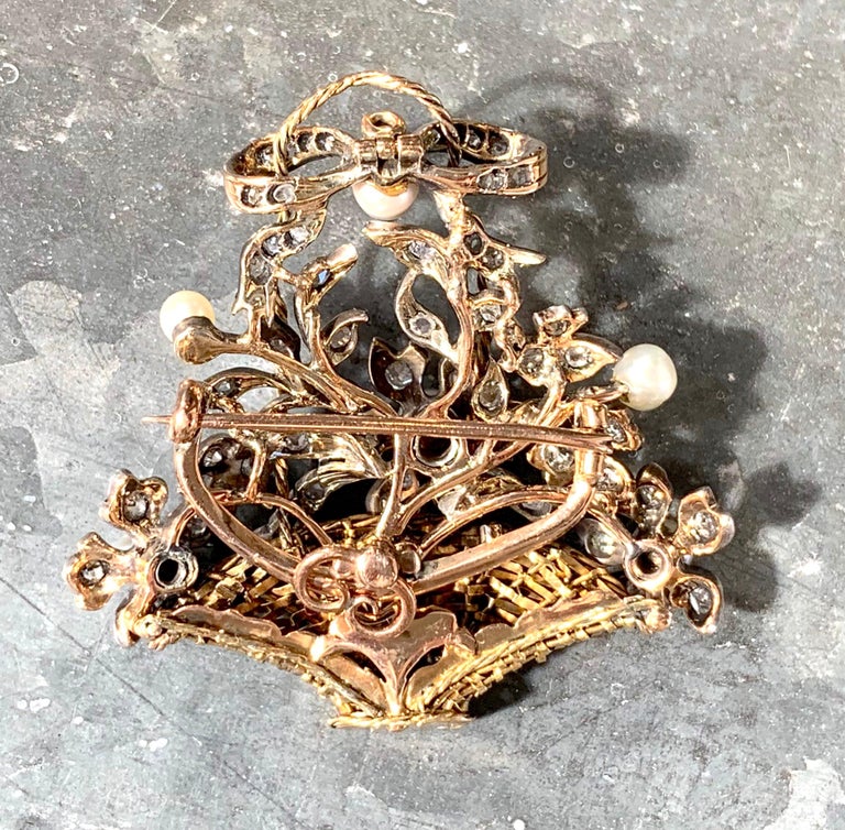 This elegant brooch is designed as an arrangement of diamond  and pearl set flowers in a braided golden handle basquet.