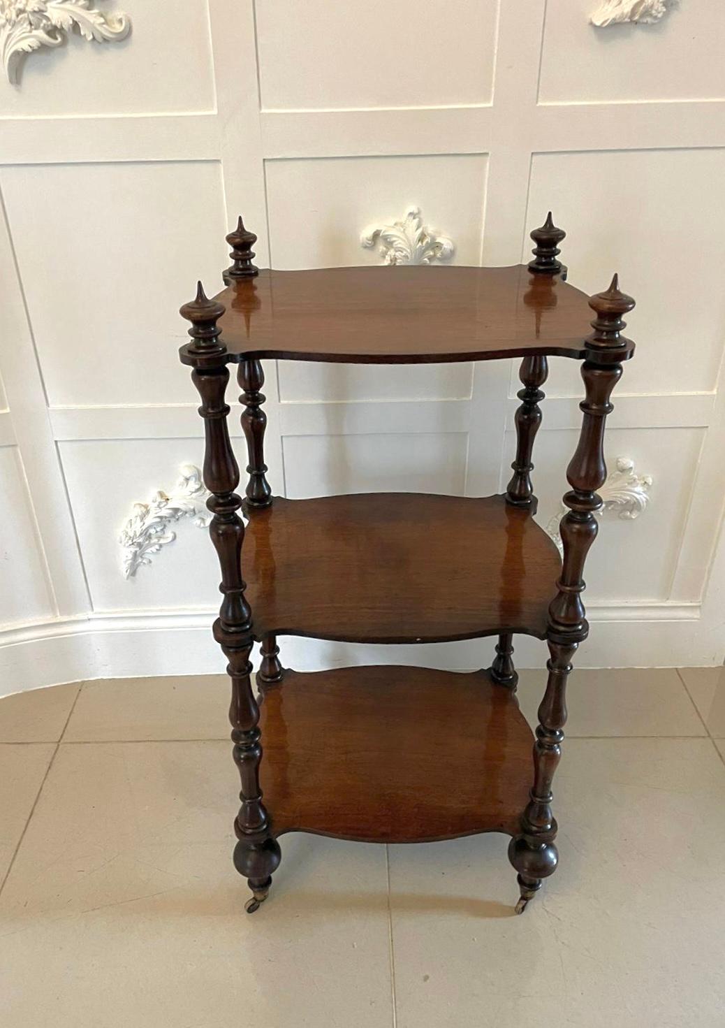 Antique Victorian freestanding rosewood whatnot having three serpentine shaped rosewood shelves supported by eight solid rosewood turned columns and four original turned finials. It stands on turned feet with original brass cup castors.

An