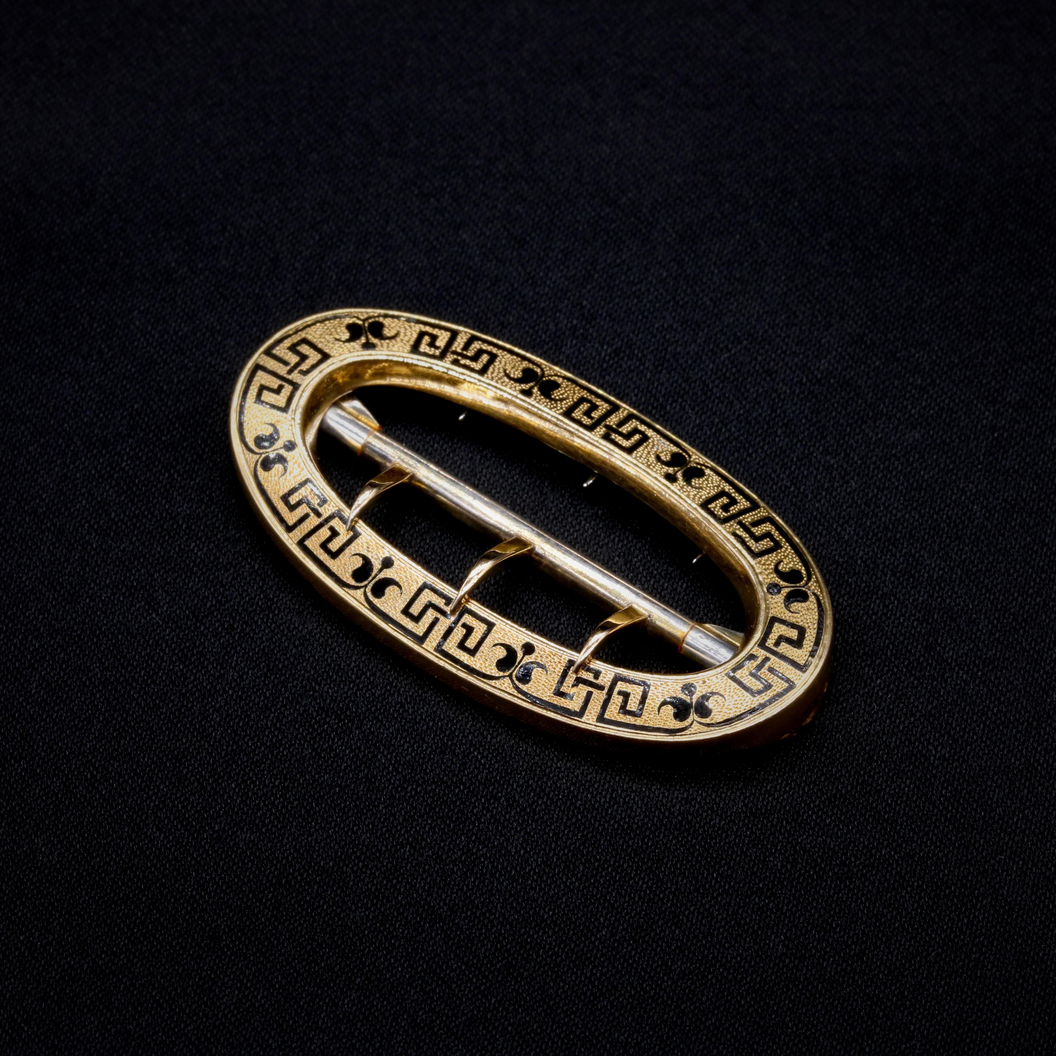 A Victorian black enamel, yellow gold, and silver belt buckle, comprising one yellow gold oval panel, adorned with black enamel, with silver buckle mechanism. 

This striking Victorian buckle would have been used to fasten a belt at the waist,