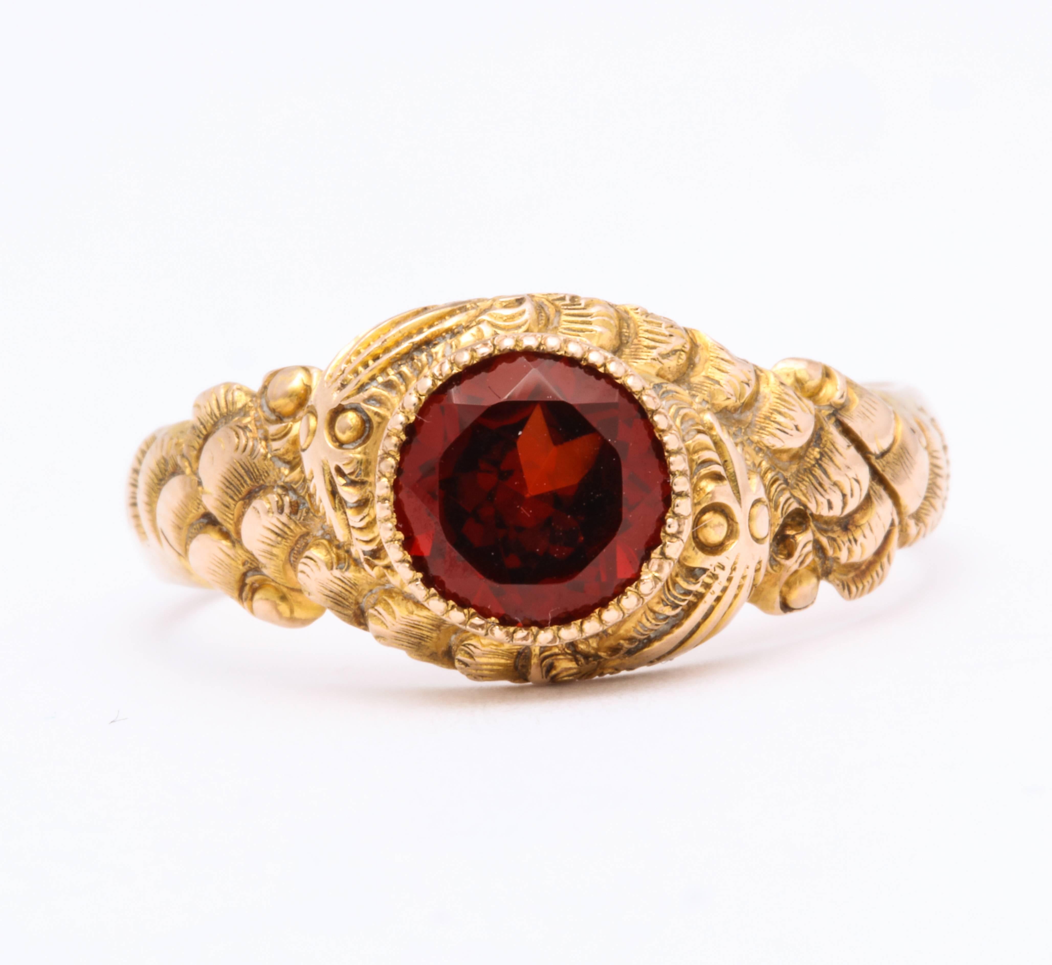 The garnet chosen for this double snake ring is a glowing, brilliant red , surrounded by two repousse engraved serpents that wrap themselves around the stone winding their way on to the substantial shank of 10 Kt gold. The entwined serpents are like