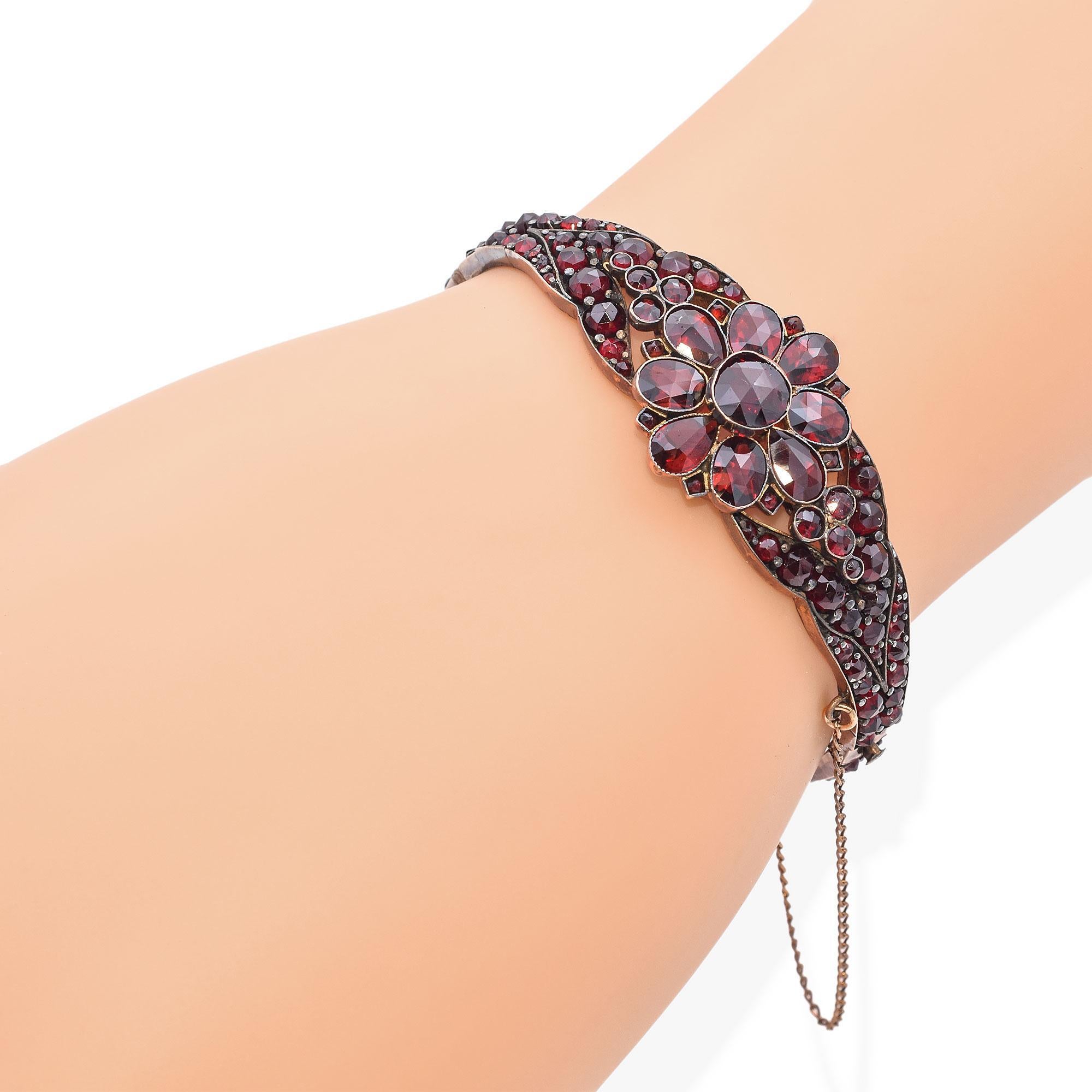 Un bracelet captivant avec un motif floral orné de pierres précieuses d'un rouge profond. Le design complexe met en valeur une fleur centrale composée de pierres rondes et en forme de poire, entourée de pierres plus petites qui s'étendent le long de