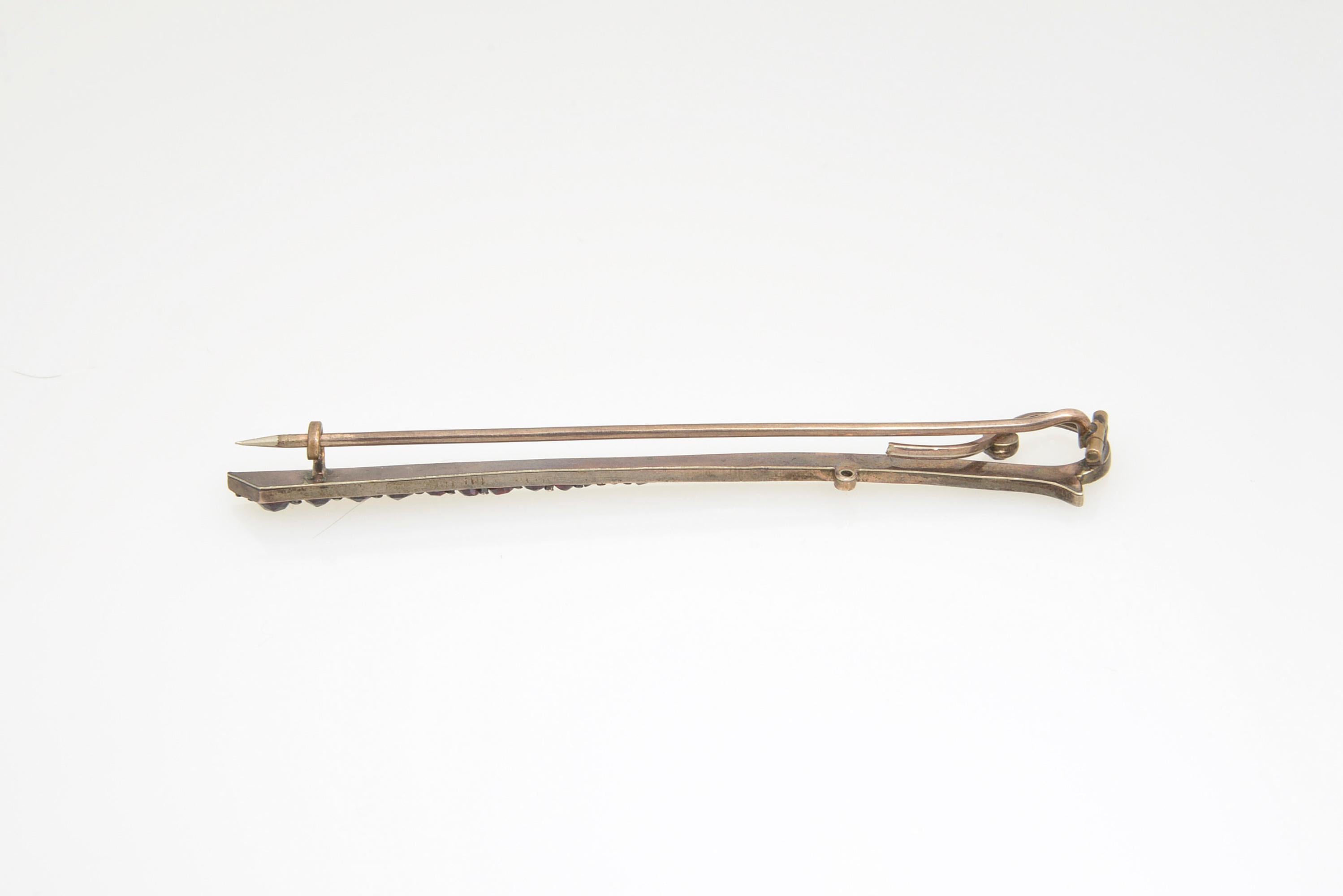 Broche victorienne antique en forme de cravache accentuée de grenats de bohème sertis dans du métal de base.