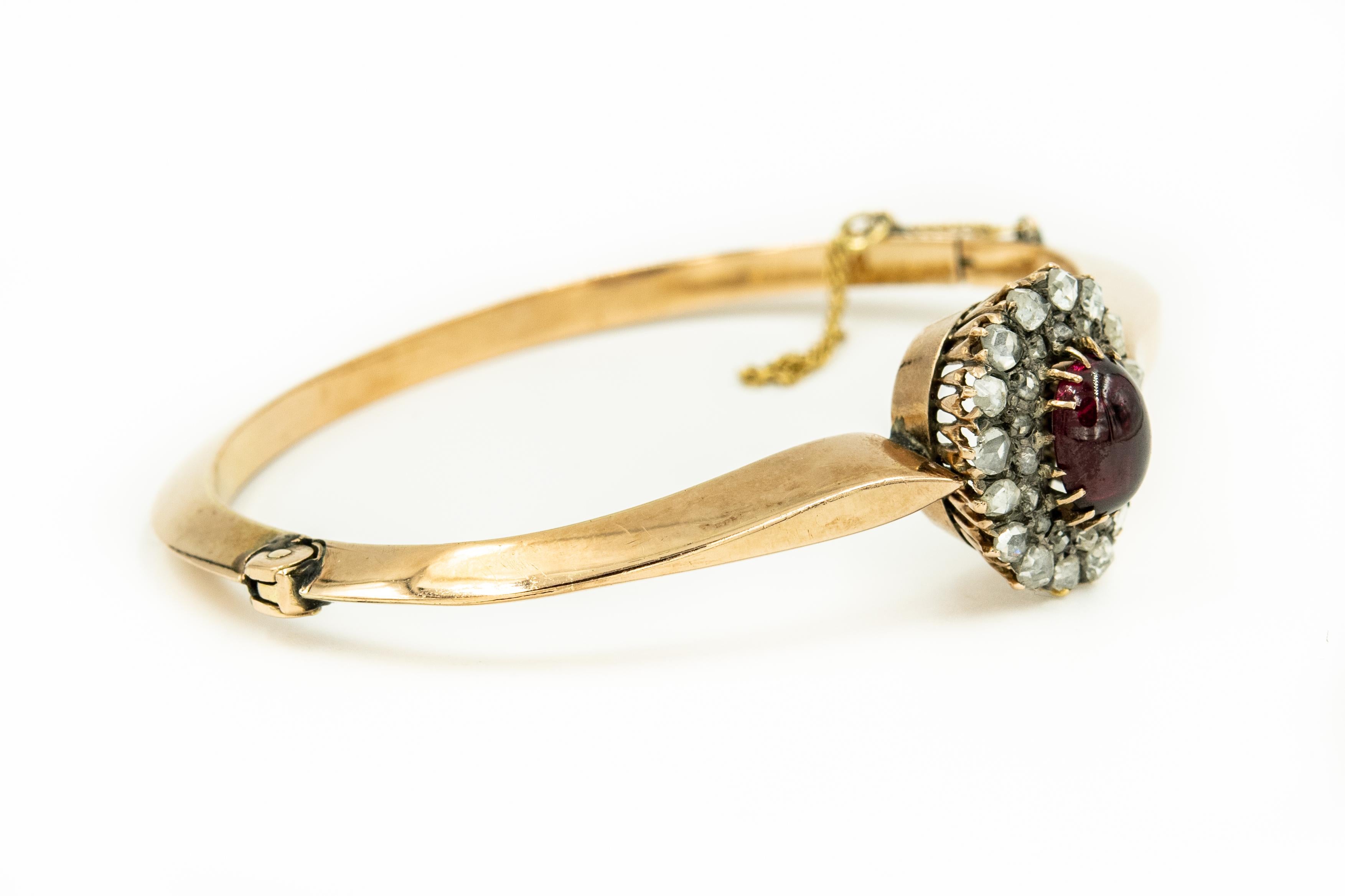 Antique Victorian 10k gold bangle bracelet featuring a centrally set oval garnet cabochon in the center of a double row rose cut diamond frame accented.  The 10k yellow gold bracelet is a knife edge design.  It has a push button and hinges open as