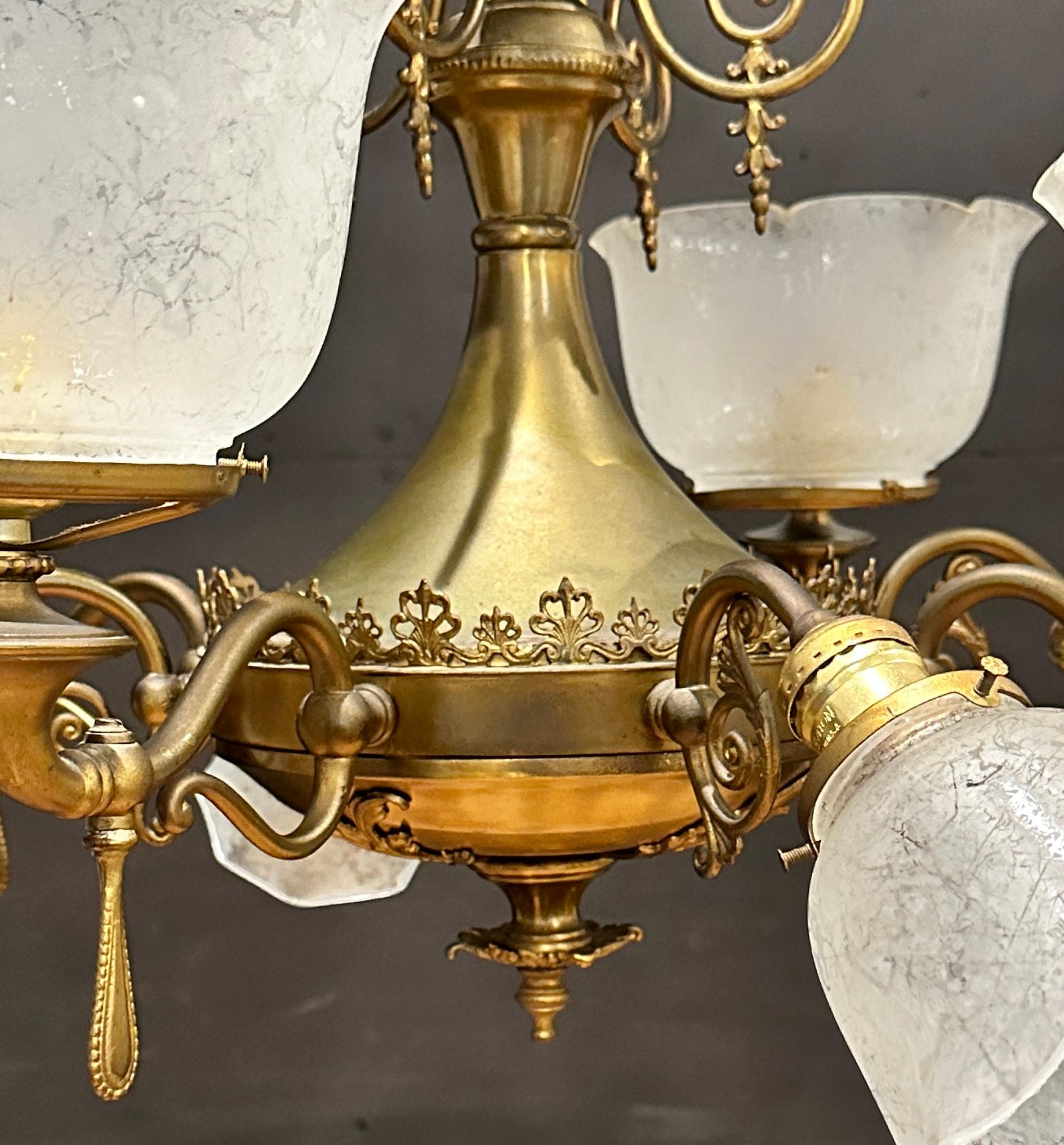 An antique Victorian gas and electric chandelier offers brass frame with scroll form up and down arms terminating in lights having glass shades, electrified, c1910.
A Victorian, brass chandelier with eight alternating between four larger up lights