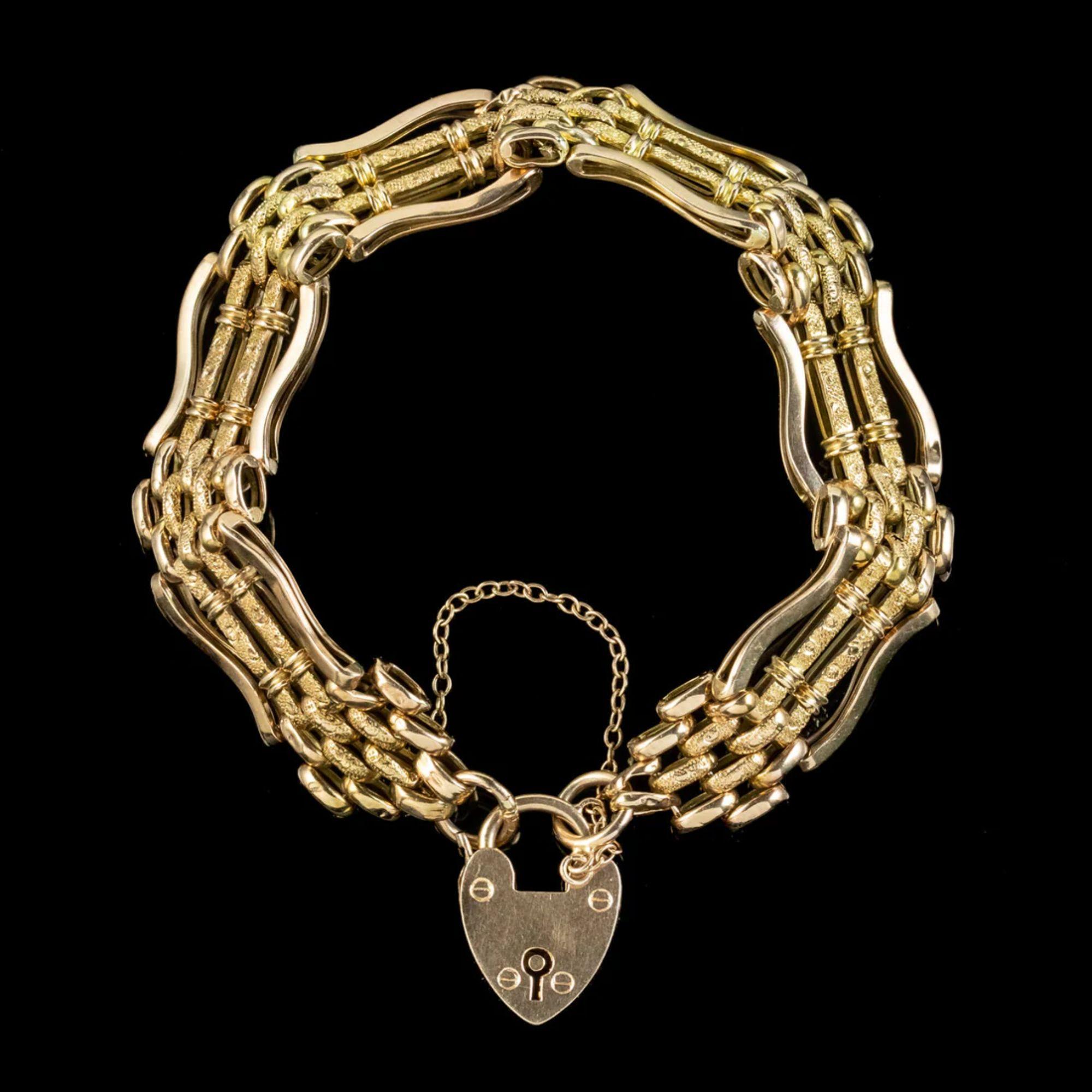 A romantic antique Victorian gate bracelet from the late 19th Century fashioned entirely in 9ct gold. The band consists of curved gate links etched with textured patterning across the centre and are held by a safety chain and heart padlock clasp,