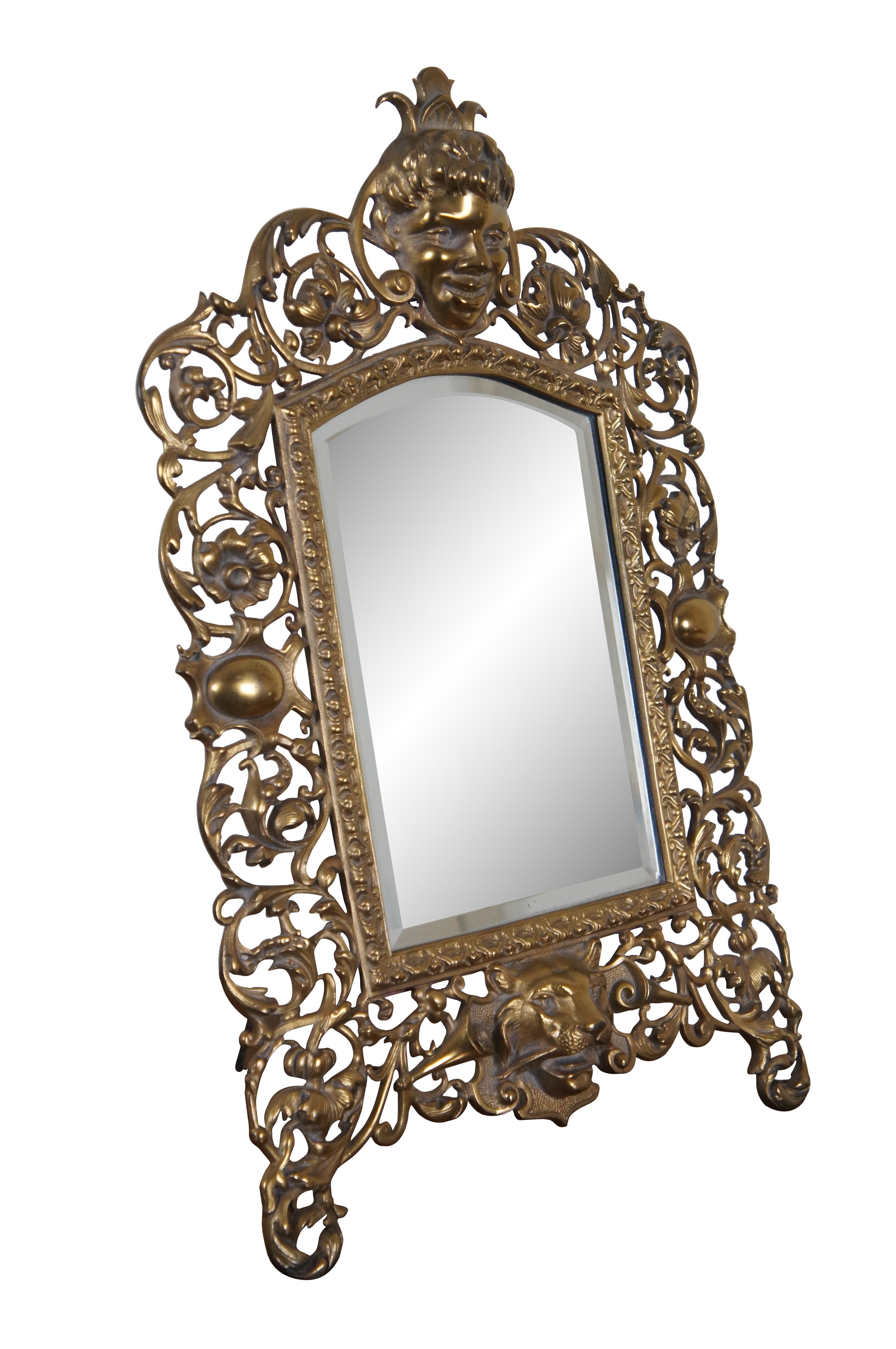 A large and heavy antique Victorian tabletop or wall hanging beveled vanity mirror.  Made of gilded cast iron featuring reticulated or pierced baroque / rococo style with floral acanthus swags, trumpets, and Lion and Cherub