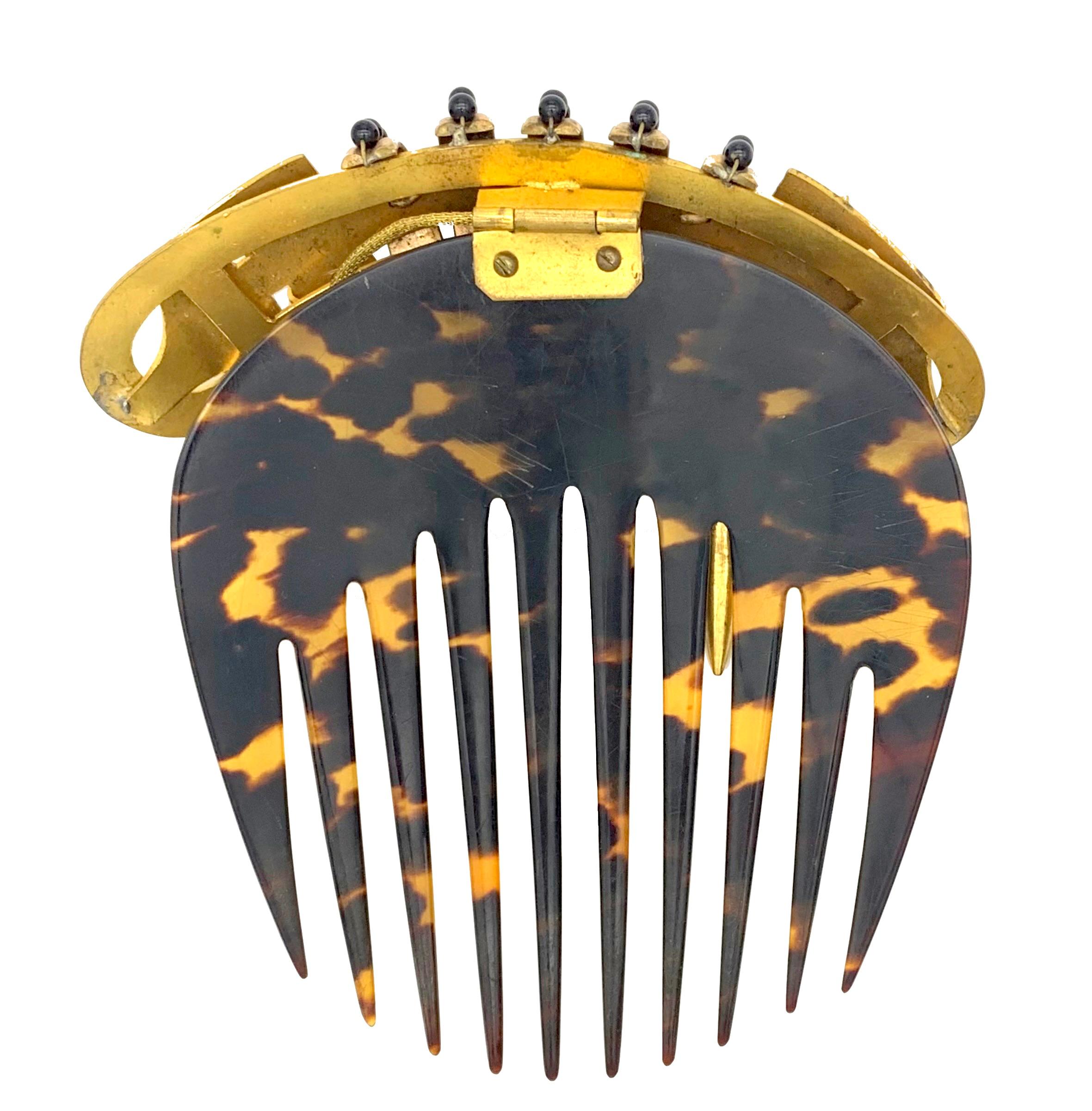 This unusual hair comb is made out of gilt metal and features a buckle motif. It is decorated with a  ball and a cone suspended from fine snake link chains. 
