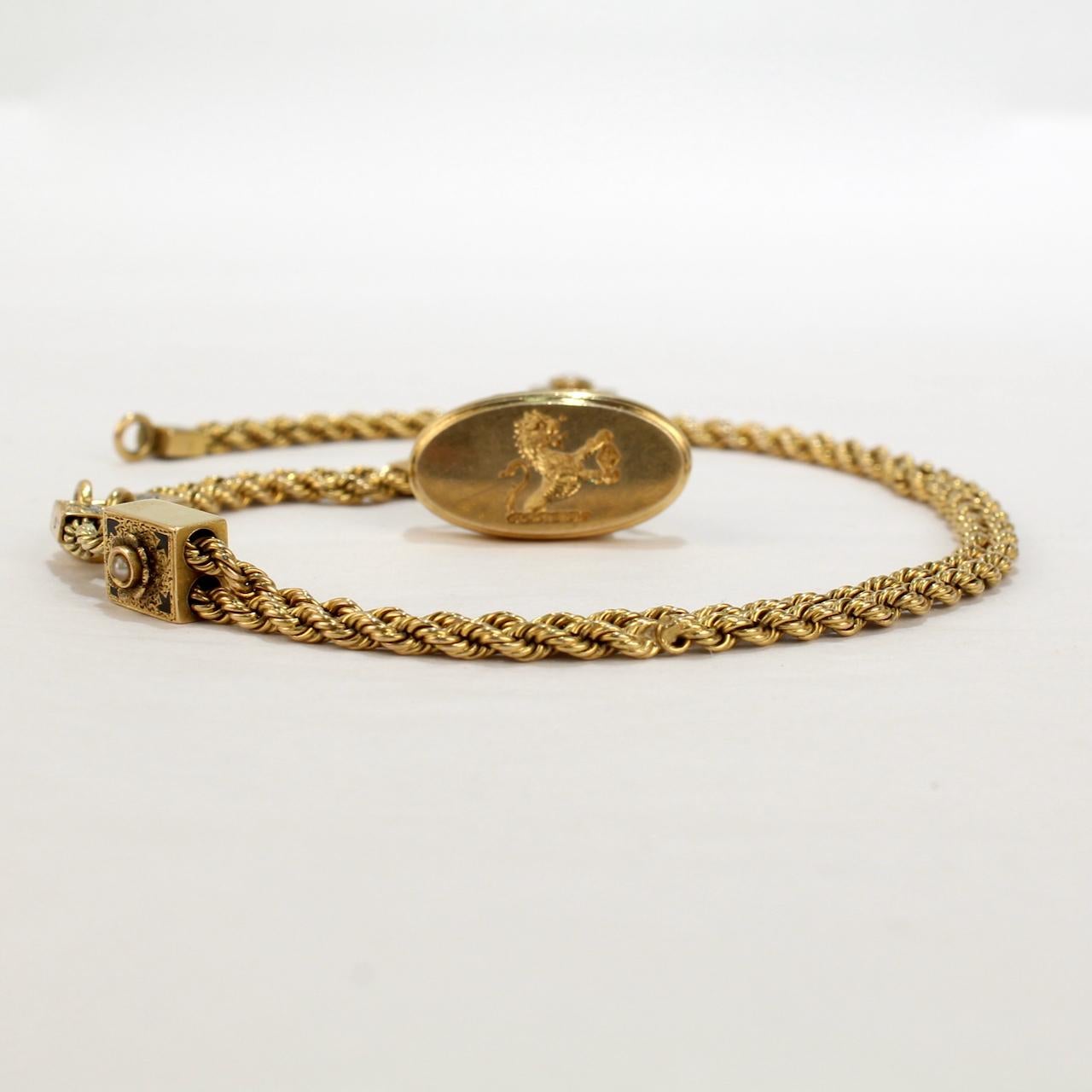 A very fine Victorian 14k gold and enamel watch chain with slides and a fob seal.

Comprised of a 14k gold rope chain with a decorative enameled gold slide and caps. 

A seal is attached with a jump ring to the end of the chain and bears an engraved