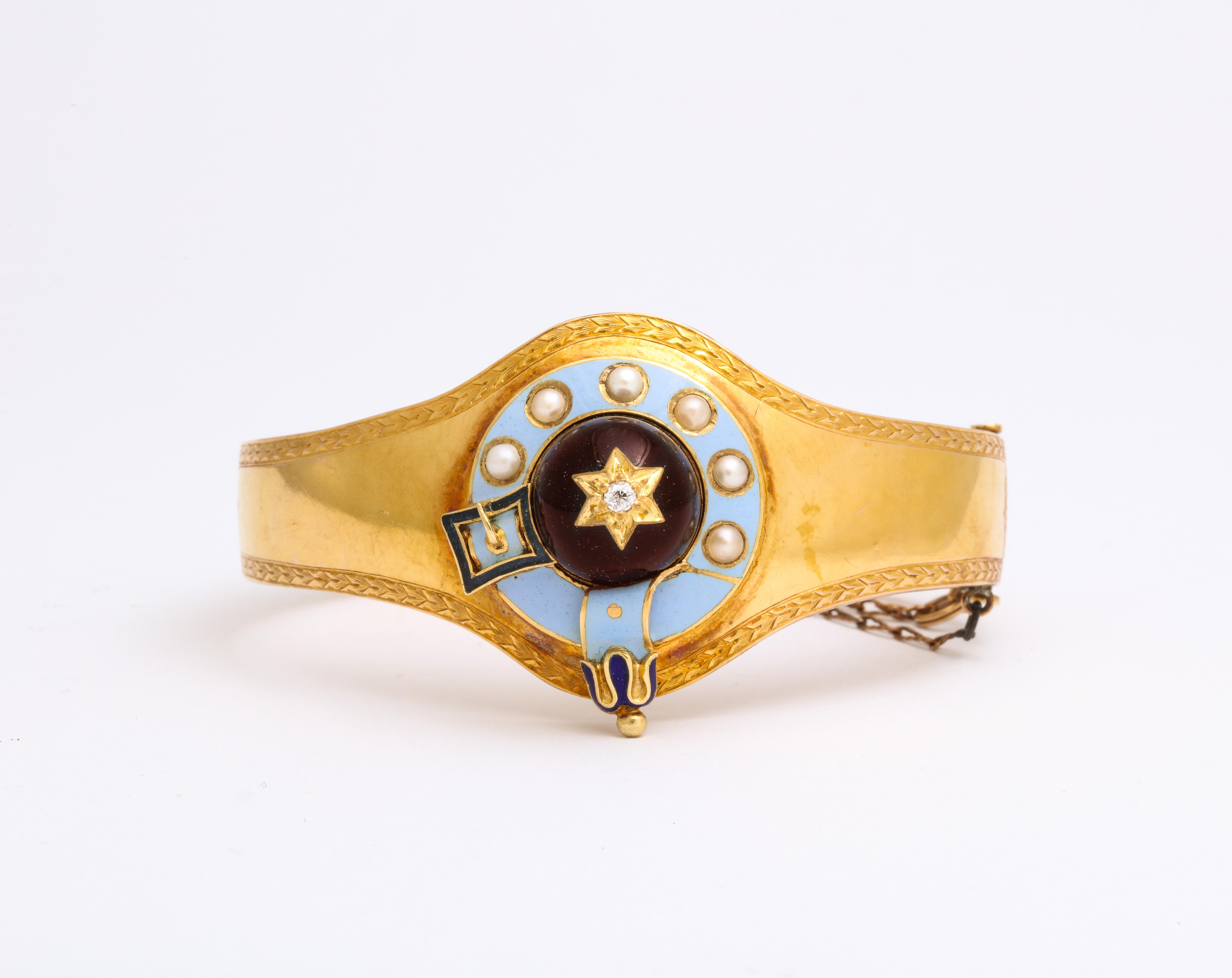 A Victorian bracelet in 15 Kt gold has a large dome cabochon garnet in the center that is set with a gold star and small diamond. A border of light blue enamel surrounds the garnet and that is set with natural pearls. A deep blue buckle and strap