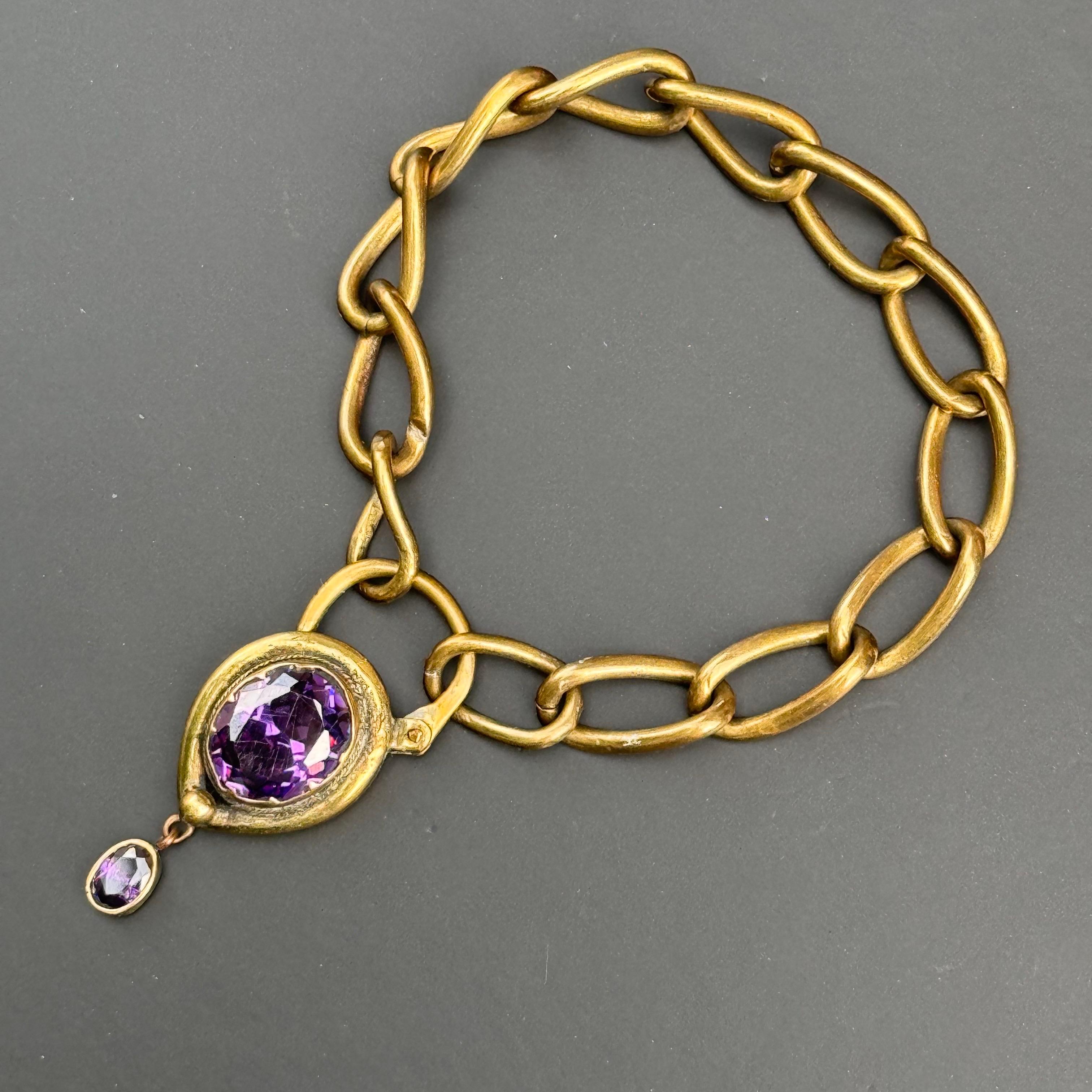 Adoptez l'élégance victorienne avec ce superbe bracelet ancien. Doté d'une large chaîne plaquée or et d'une breloque cadenas en forme de cœur ornée d'un cabochon en verre améthyste facetté, il évoque le romantisme de la fin du XIXe siècle et du