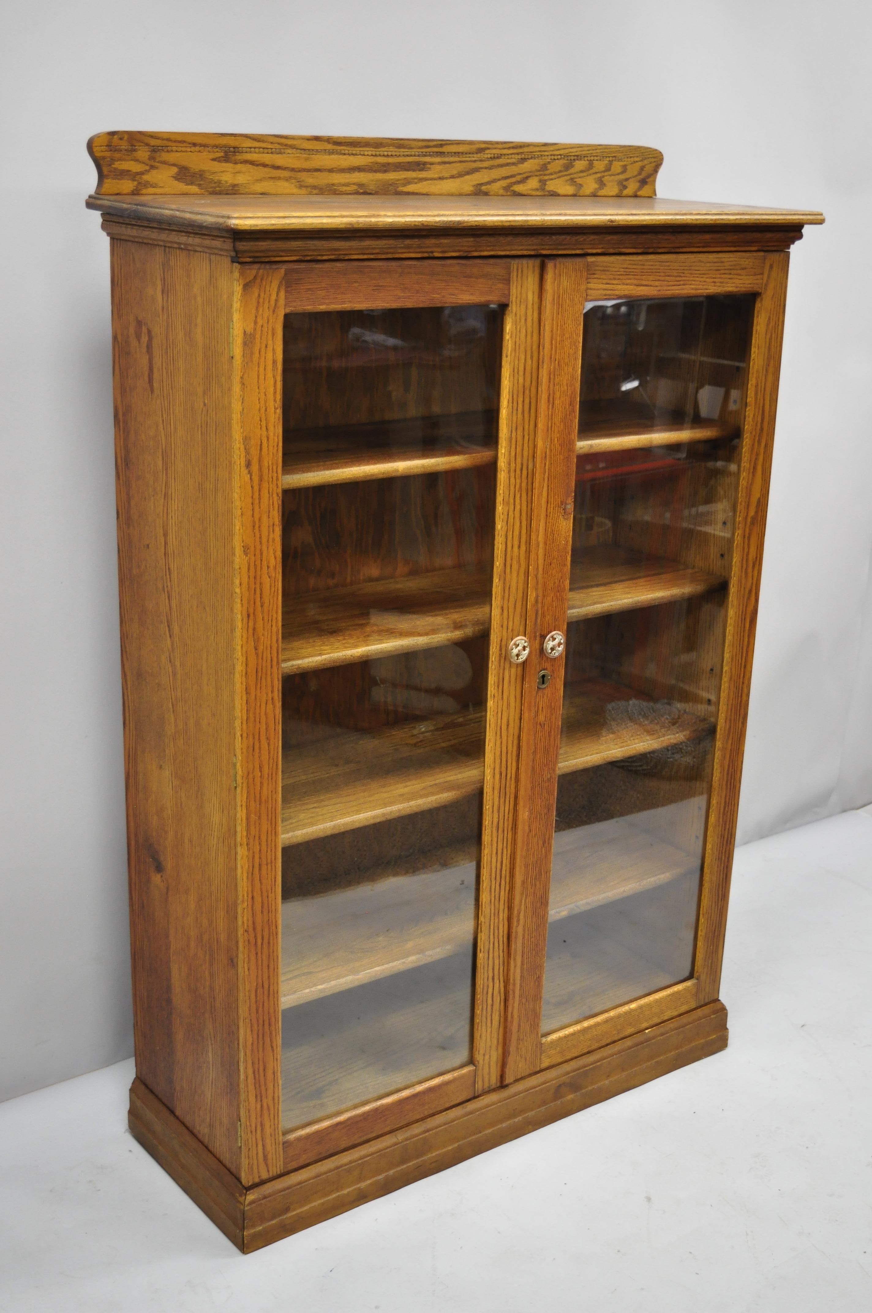 Antique Victorian golden oak glass 2 door bookcase China cabinet. Item features wood construction, beautiful wood grain, 2 swing doors, no key, but unlocked, 4 adjustable shelves, very nice antique item. circa early 1900s. Measurements: 57