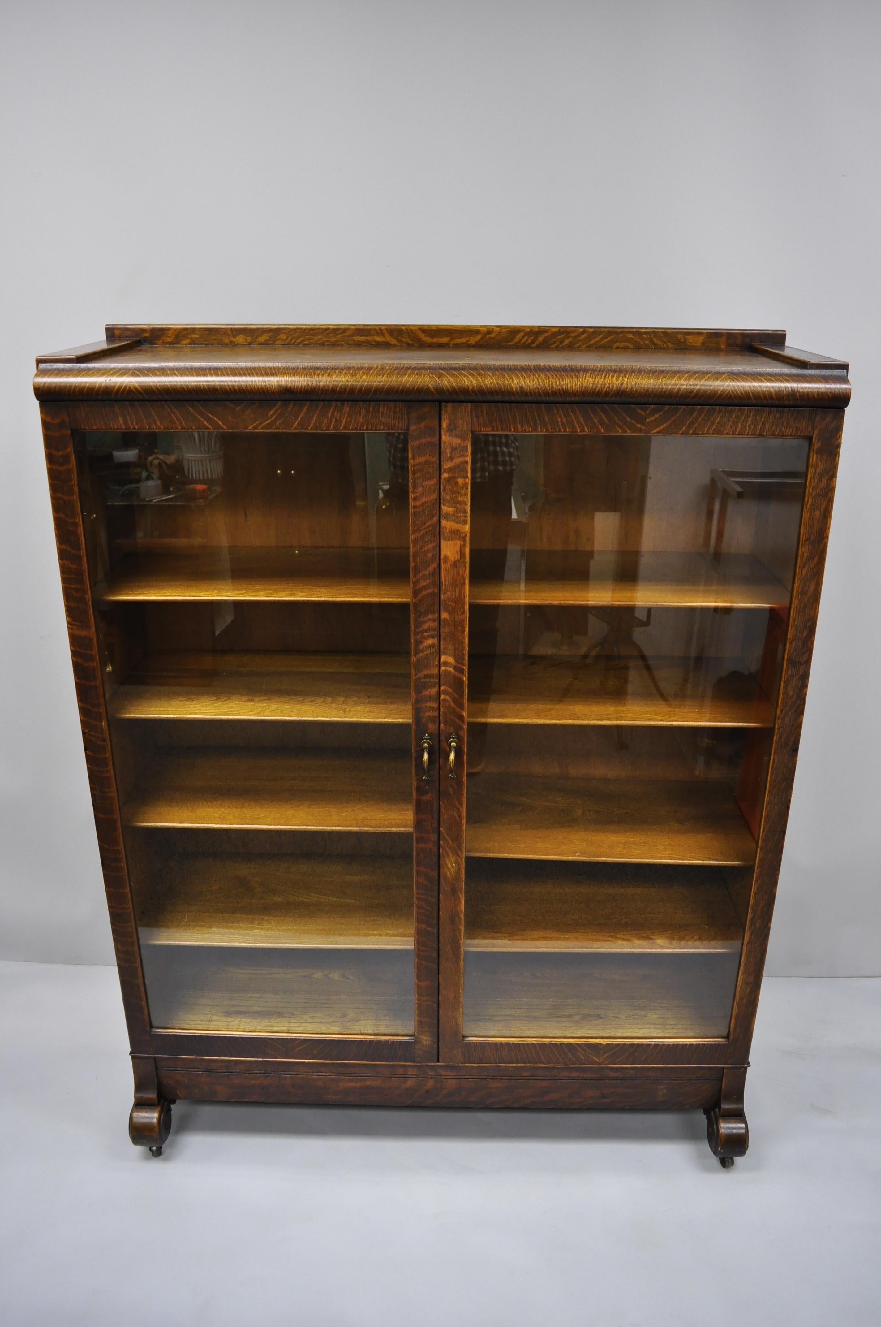 Antique Victorian golden tiger oak glass double door china cabinet bookcase. Item features rolling casters, beautiful wood grain, two swing doors, eight adjustable shelves, quality American craftsmanship. circa early 20th century. Measurements: 60