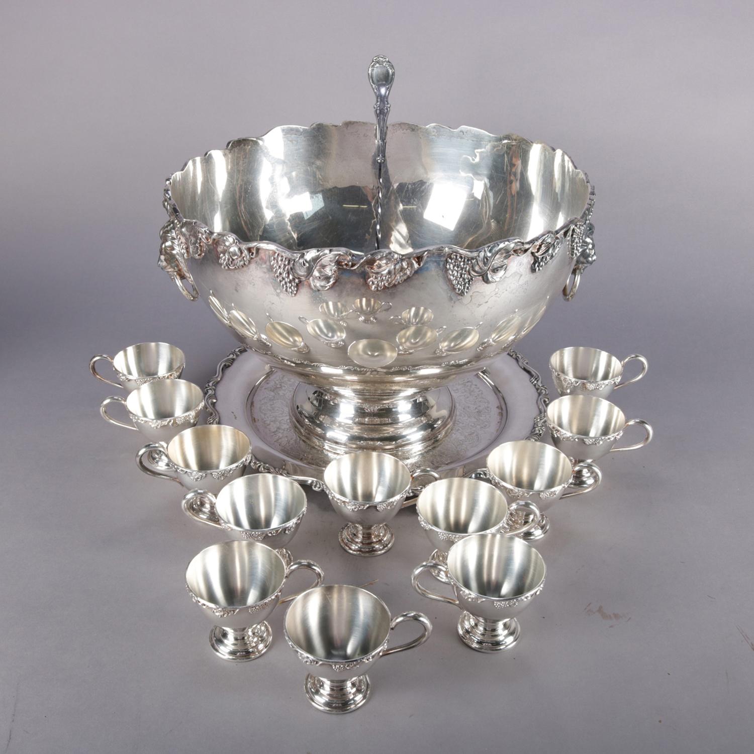 Antique Victorian silver plate punch bowl set features bowl with scalloped rim having high relief grape and leaf decoration with two lion mask handles and raised on column base with underplate, set with 12 grape and leaf pedestal cups and ladle, en