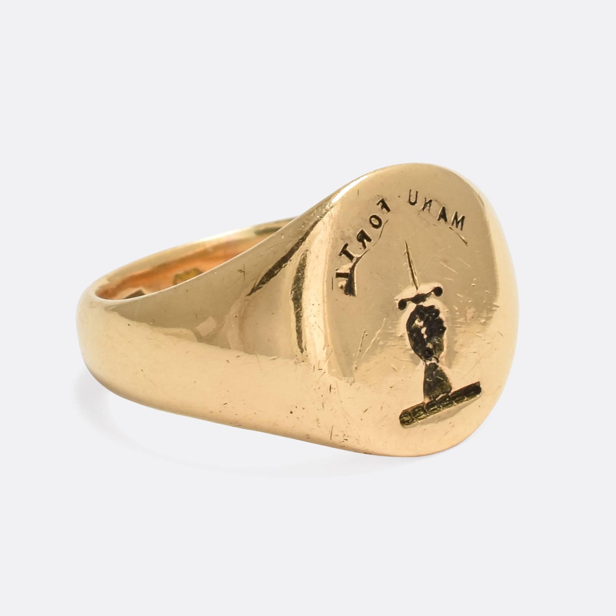 A cool antique signet ring modelled in 18 karat gold. The face is engraved with an English Heraldic crest, depicting a hand holding a dagger above the Latin motto MANU FORTI, meaning 