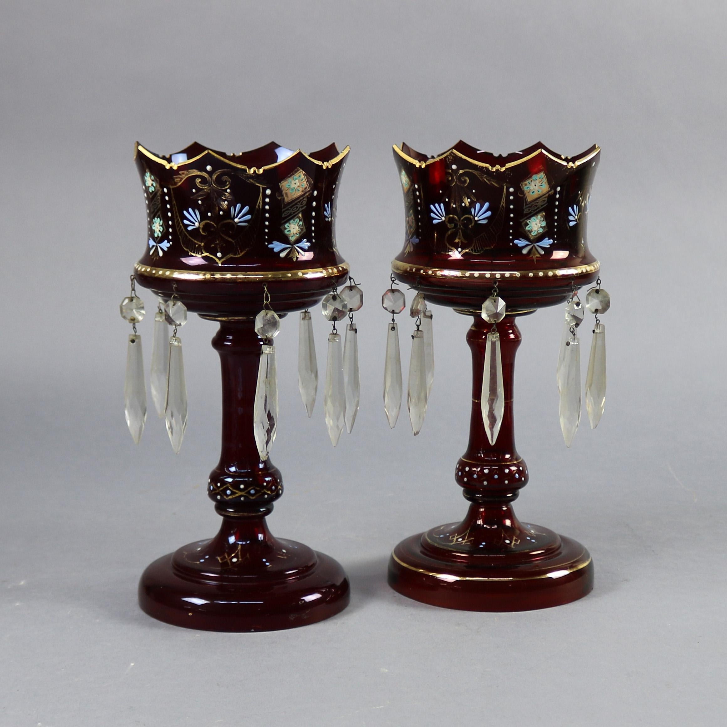 An antique pair of Victorian King & Queen Bohemian style mantel lustres feature cranberry glass construction with bowls in crown form, hand painted with floral motif and and having hanging crystal prisms, gilt highlights throughout, circa