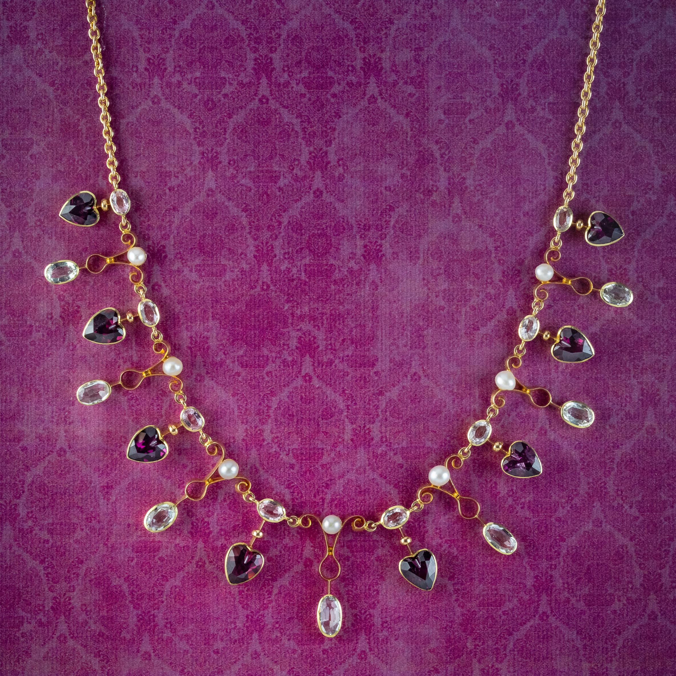A magnificent antique Victorian dropper necklace from the late 19th Century adorned with fifteen droppers adorned with alternating blue oval cut aquamarines and violet almandine garnet hearts, with a line of white pearls and further aquas running