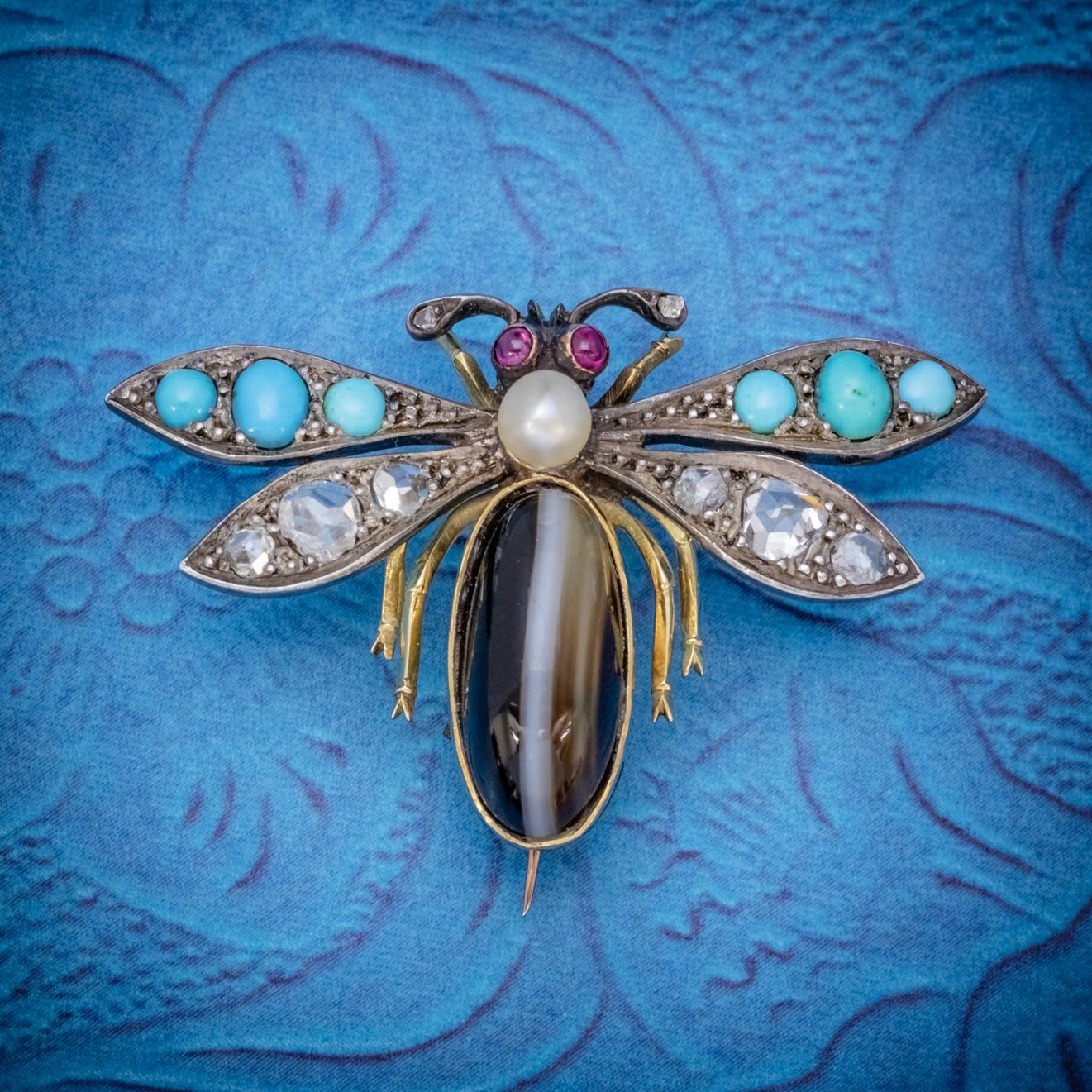 A fabulous Antique Victorian winged insect brooch set with a beautiful polished bullseye Agate abdomen leading to Turquoise and Rose cut Diamond encrusted wings, Ruby set eyes and topped with a lustrous Pearl in the centre. 

The Piece is