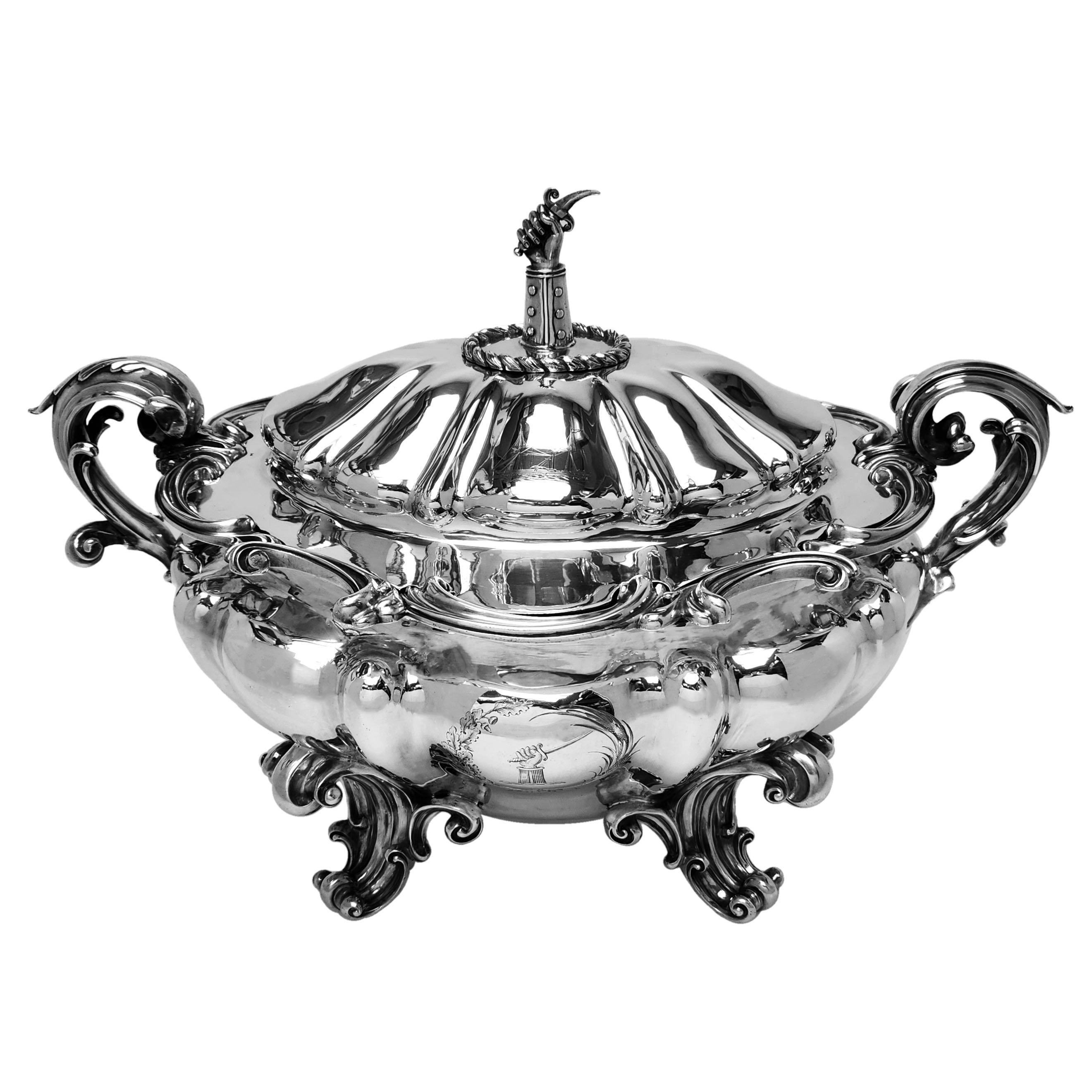 Magnífica sopera de plata antigua victoriana que descansa sobre cuatro impresionantes patas en forma de voluta y tiene un par de asas ornamentadas en forma de voluta a los lados. El cuerpo de la sopera tiene una armadura grabada en el centro de una