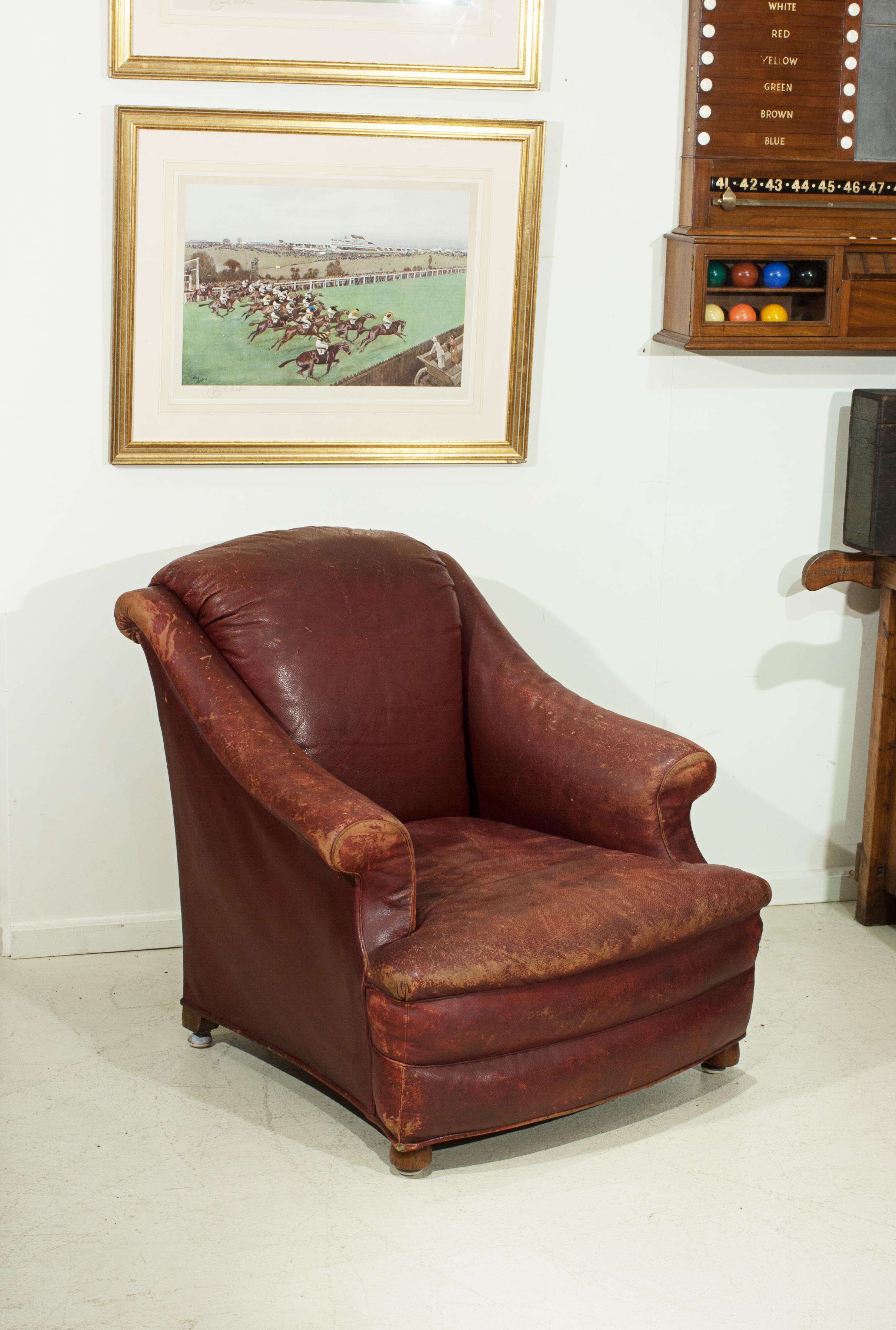 A late 19th, early 20th century leather club arm chair, with scroll-over back and arms upholstered with the original red leather. The easy chair raised on front bun feet and square rear legs, all fitted with carpet glides. The easy chair is a