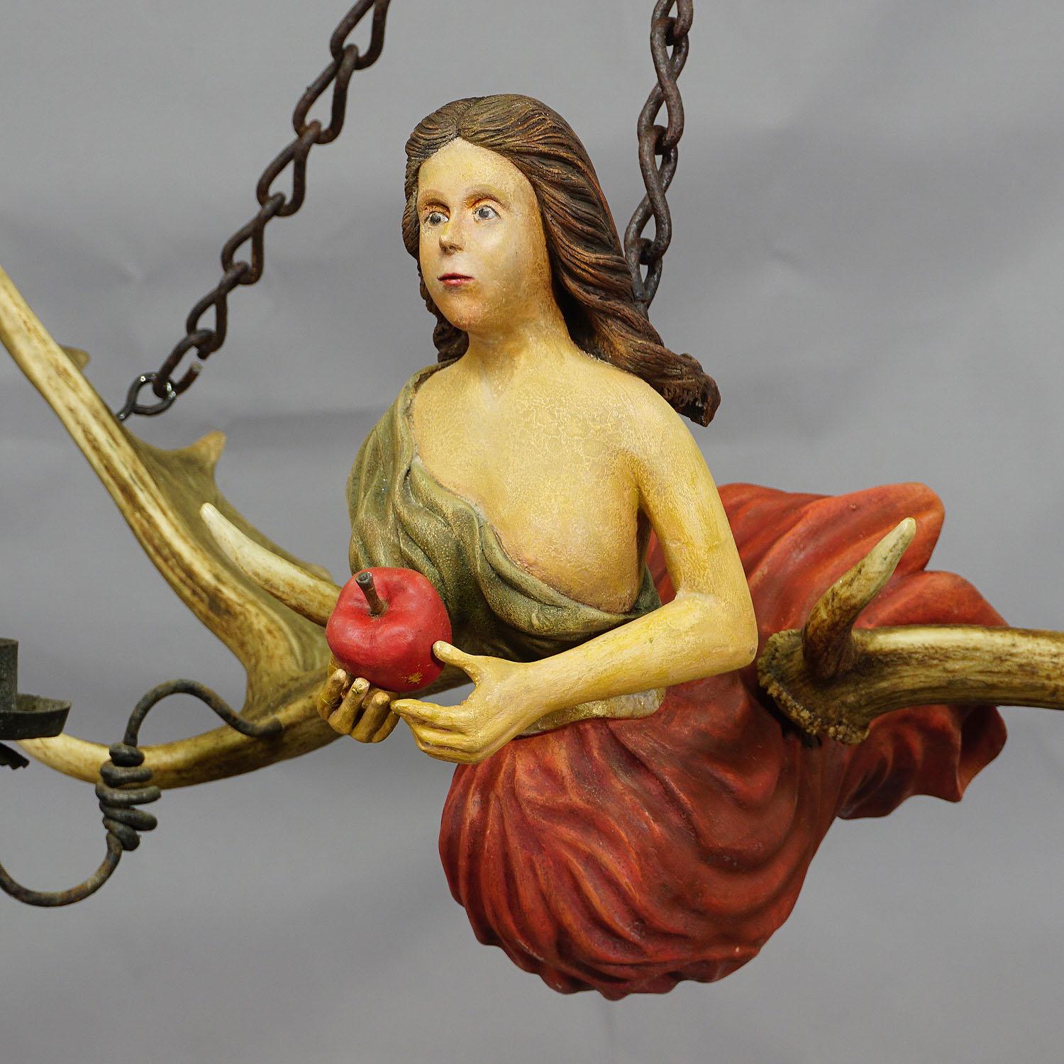 An antique lusterweibchen of a Victorian lady holding an apple. The statue is made of wood and attached to a pair of original fallow deer antlers. With iron suspension and two forged iron candle lights. Good condition, original painting was damaged