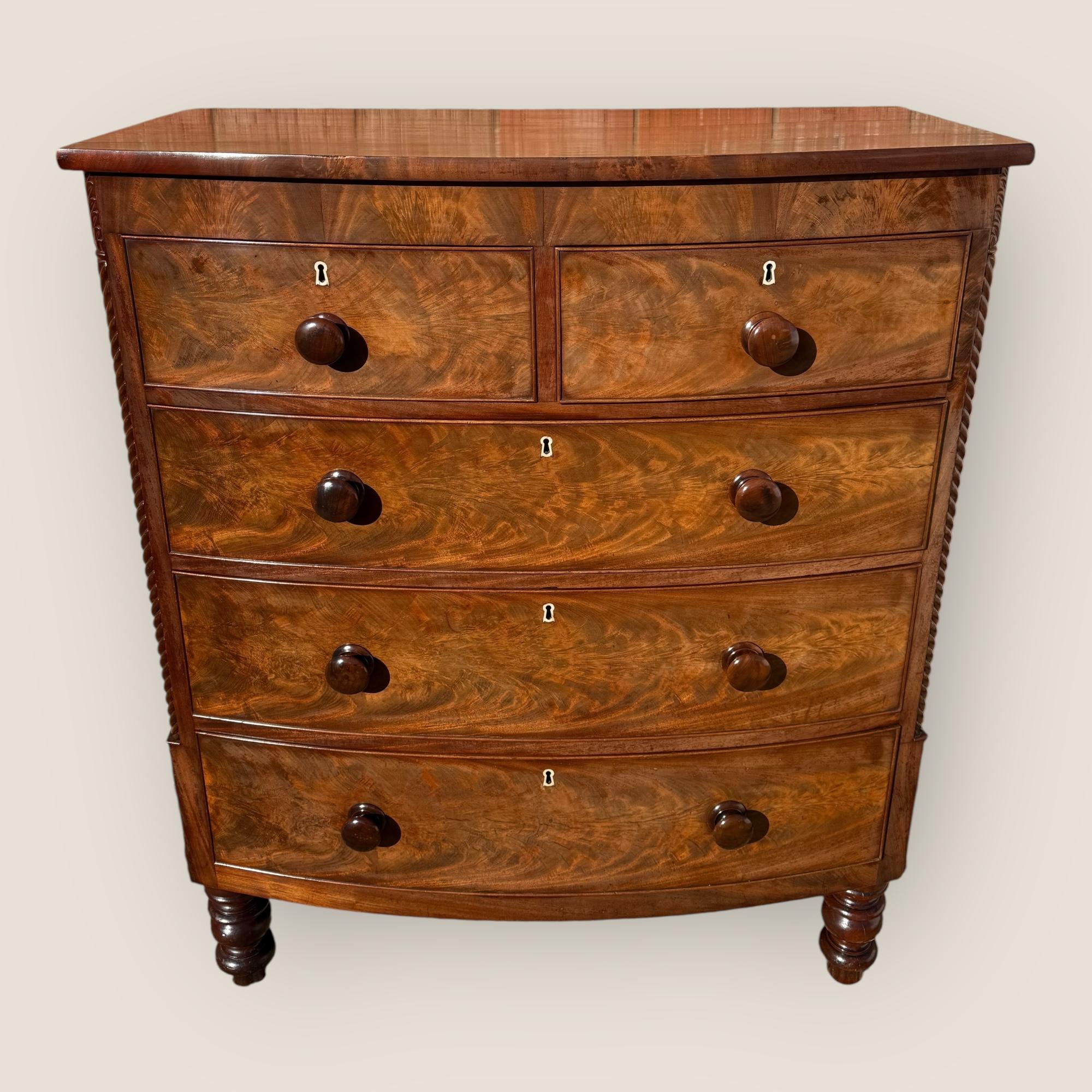 Here we have an antique mid Victorian (1850-1870) mahogany bow front chest of 2 short over 3 long drawers with wooden knob handles and ivory key inscriptions (reference number listed below). This pieces stands on 4 turned feet, and is decorated with