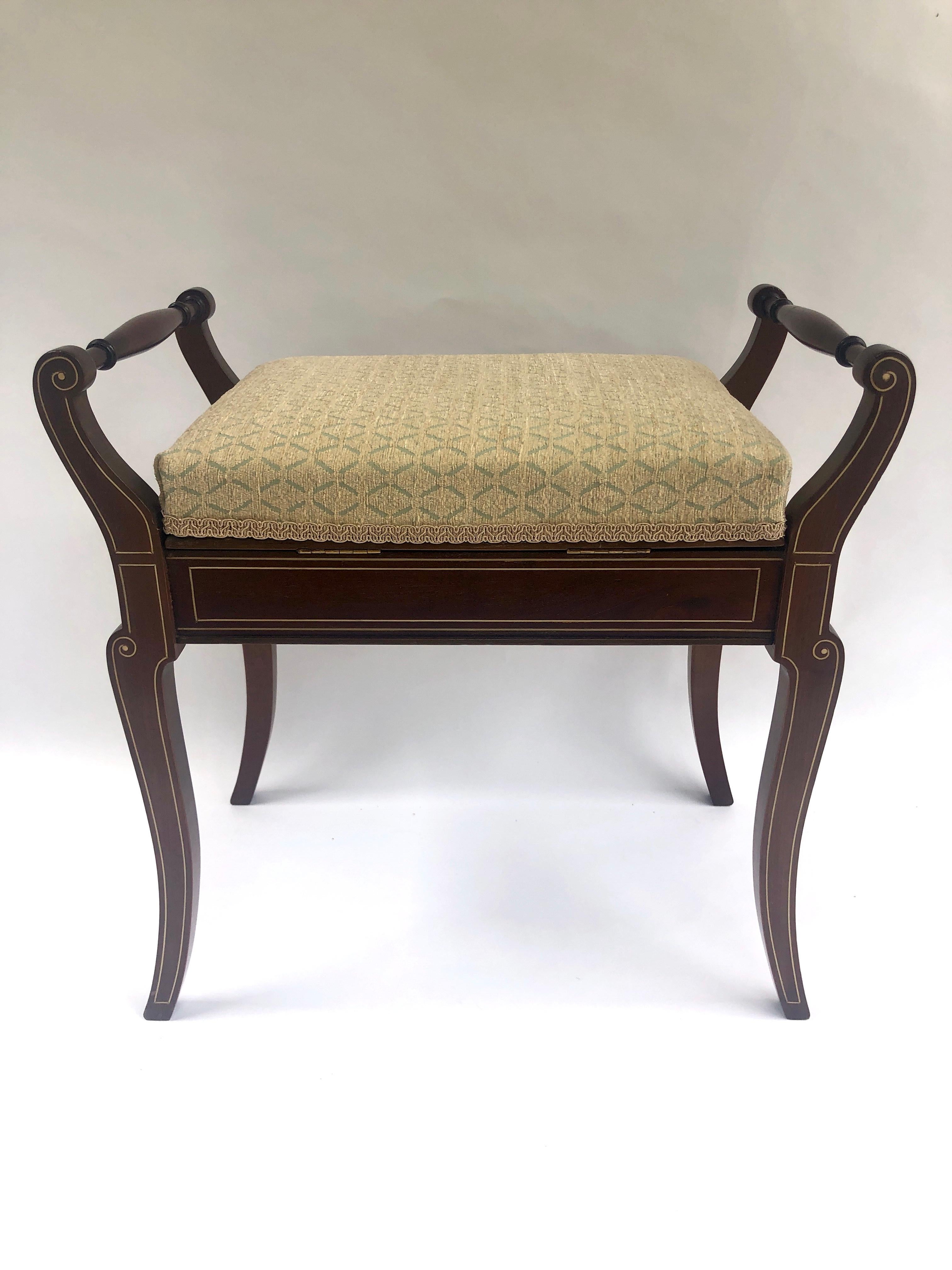 This is an exceptionally attractive antique Victorian mahogany freestanding inlaid piano stool with turned carrying handles. It features a reupholstered lift up seat revealing a storage area and pretty frieze with shell and stringing inlay, standing