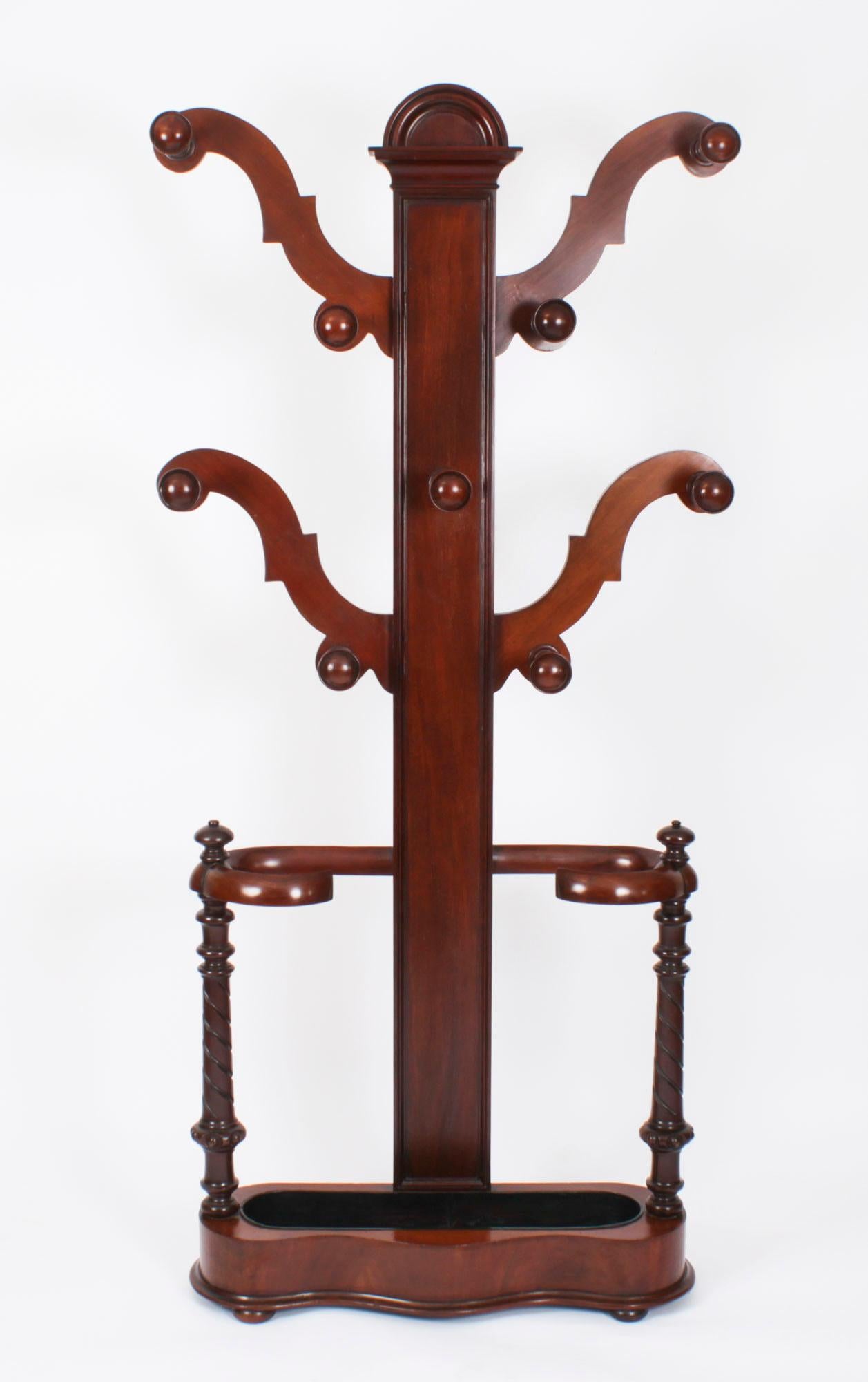 This is a stylish antique Victorian solid mahogany hall stand, circa 1860 in date. 
 
The stand features four branches and nine turned coat hooks, above a serpentine umbrella /walking stick stand with an inset metal drip tray, andraised on  bun