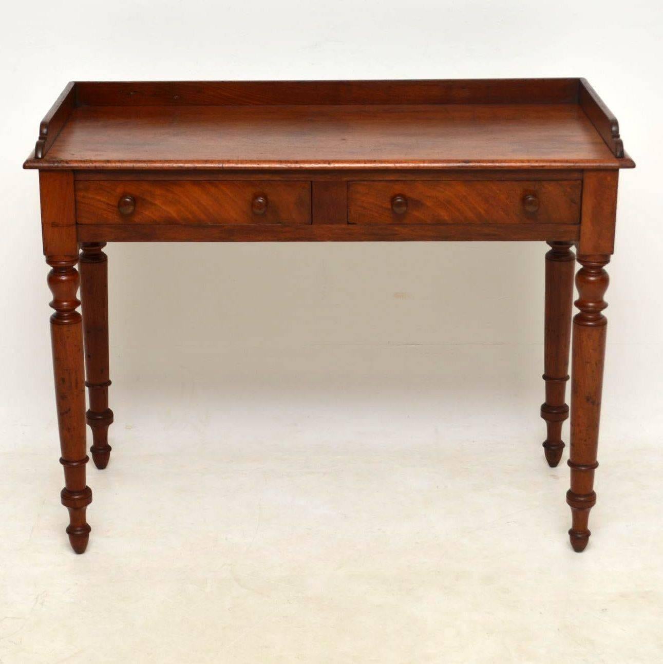 Antique Victorian mahogany writing table with the original gallery on the back and sides. It’s in good original condition, with plenty of character and natural distressing. There are two drawers with turned mahogany handles and the legs are