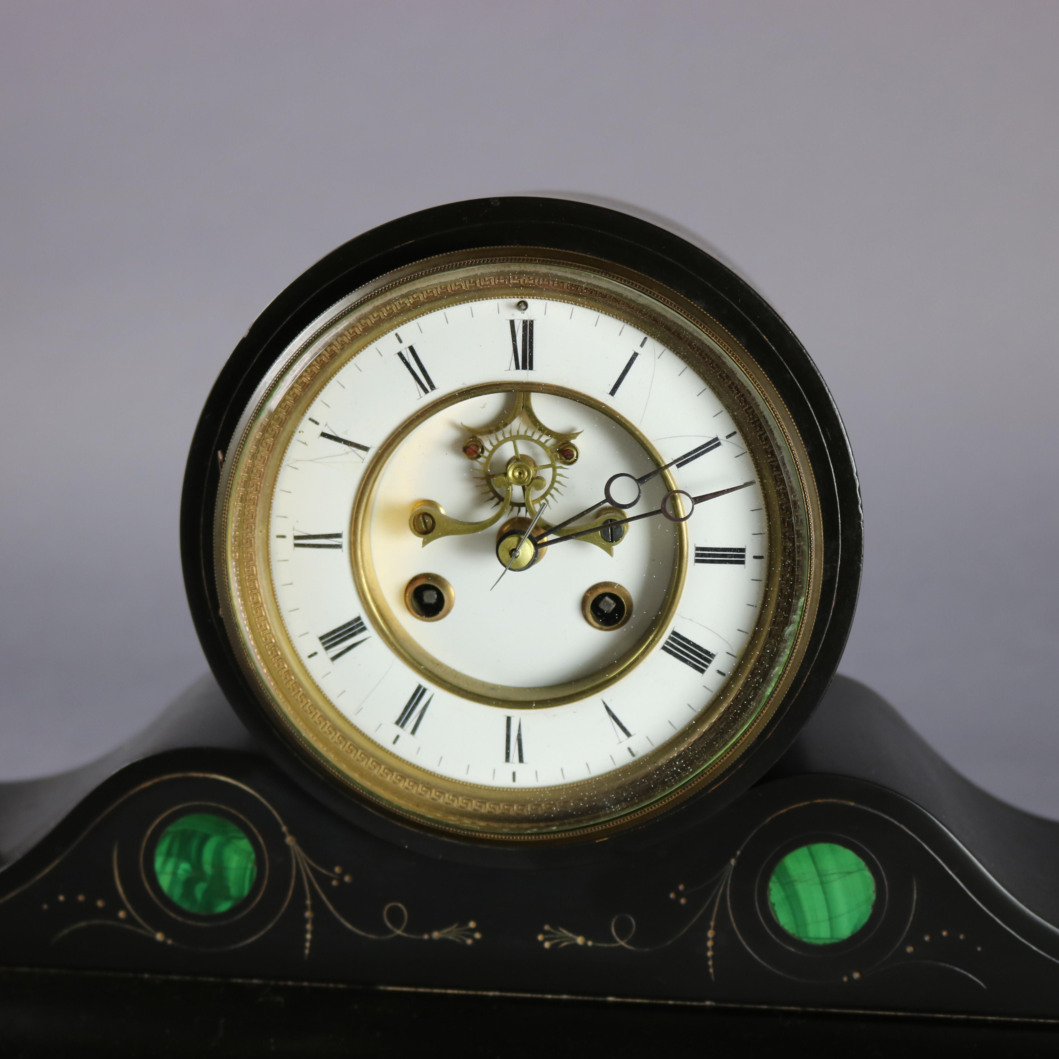 An antique Victorian mantel clock offers slate construction in stylized camel back form with malachite inlay and incised gilt scroll decoration, open escapement face with Roman numerals, working and with key and pendulum, circa 1890

***DELIVERY