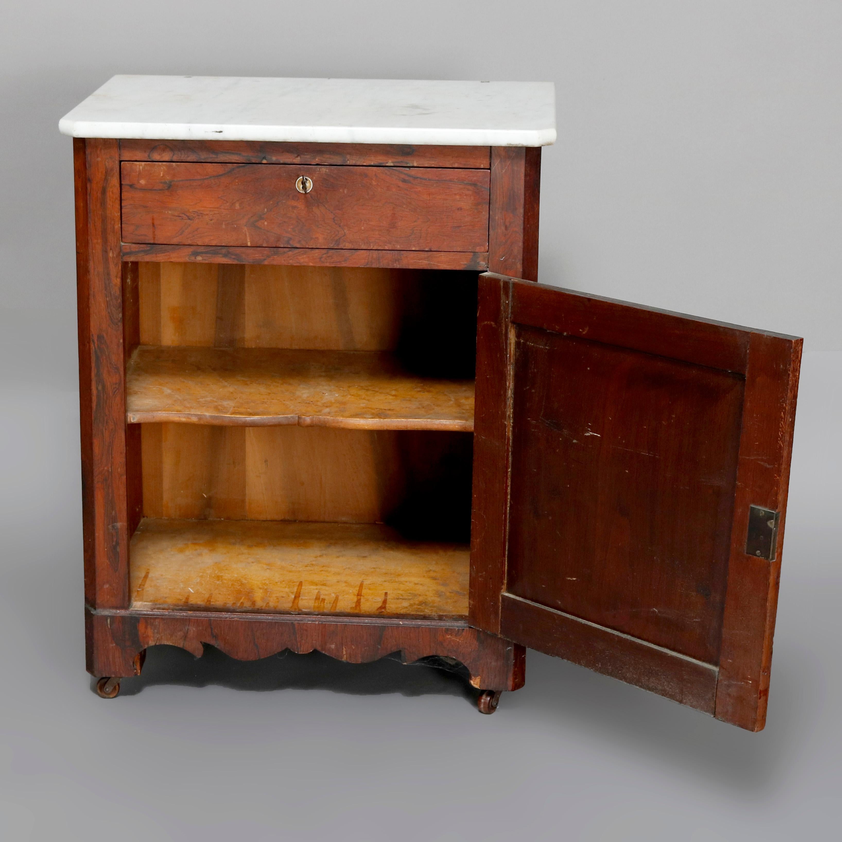 An antique Victorian half-commode offers marble top surmounting burl case with single upper drawer and lower shelved cabinet over shaped skirt and seated on casters, 19th century

Measures: 30