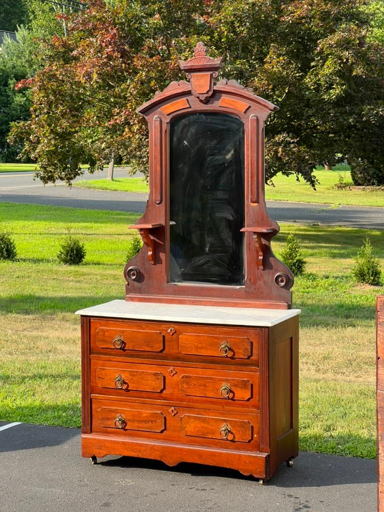 Entrez dans une époque révolue avec ce coffre victorien ancien en noyer à dessus en marbre et miroir, une pièce étonnante qui incarne la grandeur et l'artisanat détaillé de l'époque victorienne. Cette commode présente une finition noyer riche et