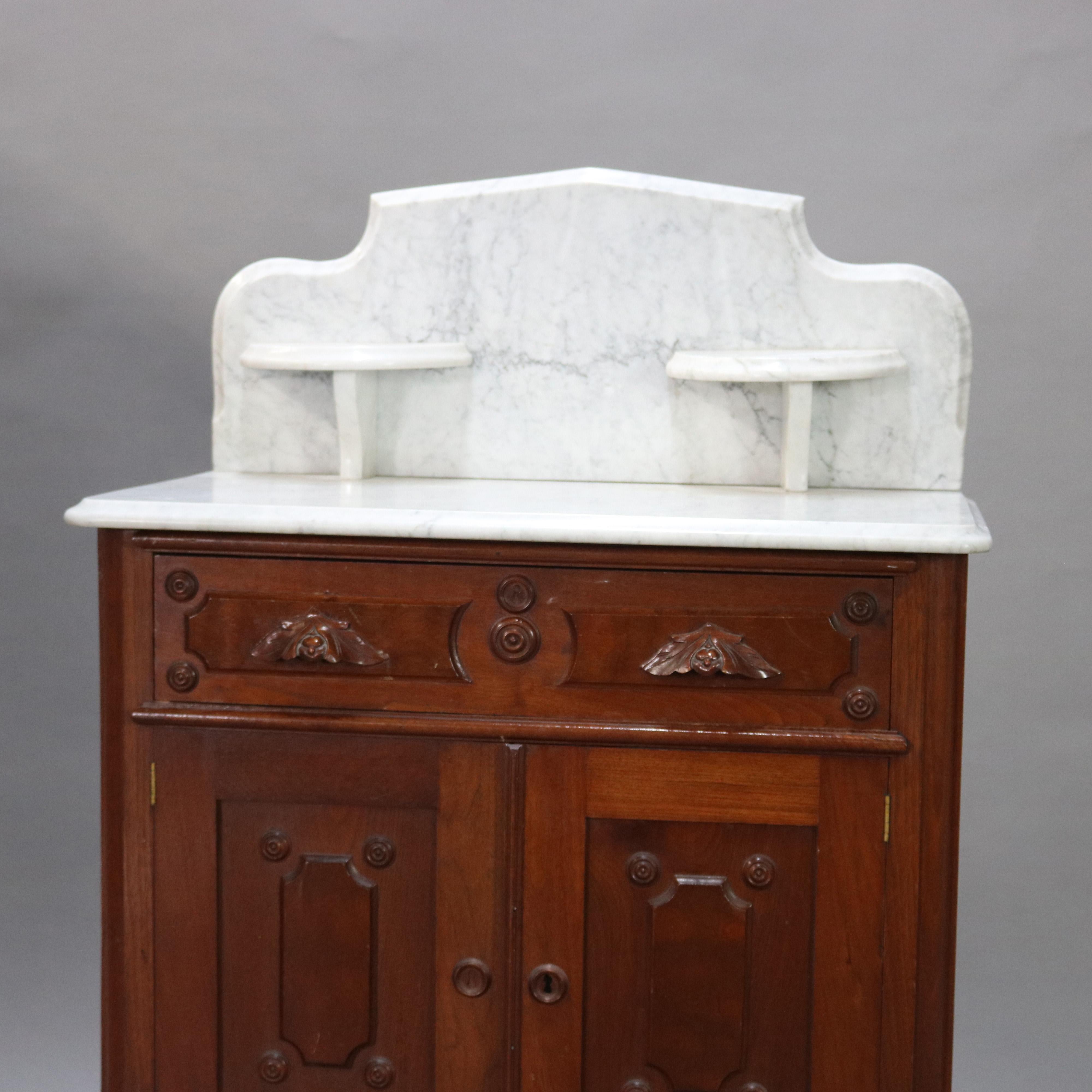An antique Victorian washstand commode offers shaped and beveled backsplash with flanking candle stands over walnut base with paneled frieze drawer having foliate carved handles over a double paneled door lower cabinet, raised on casters, circa