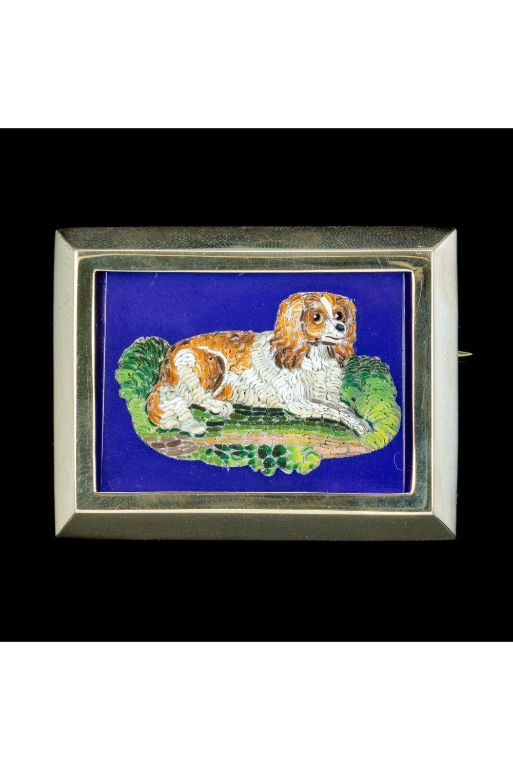 A delightful Antique Victorian Micro Mosaic depicting an adorable King Charles Spaniel laid upon a bed of green grass. The level of detail is astonishing, with realistic colouring and shading inlaid expertly into the blue setting by a true master of