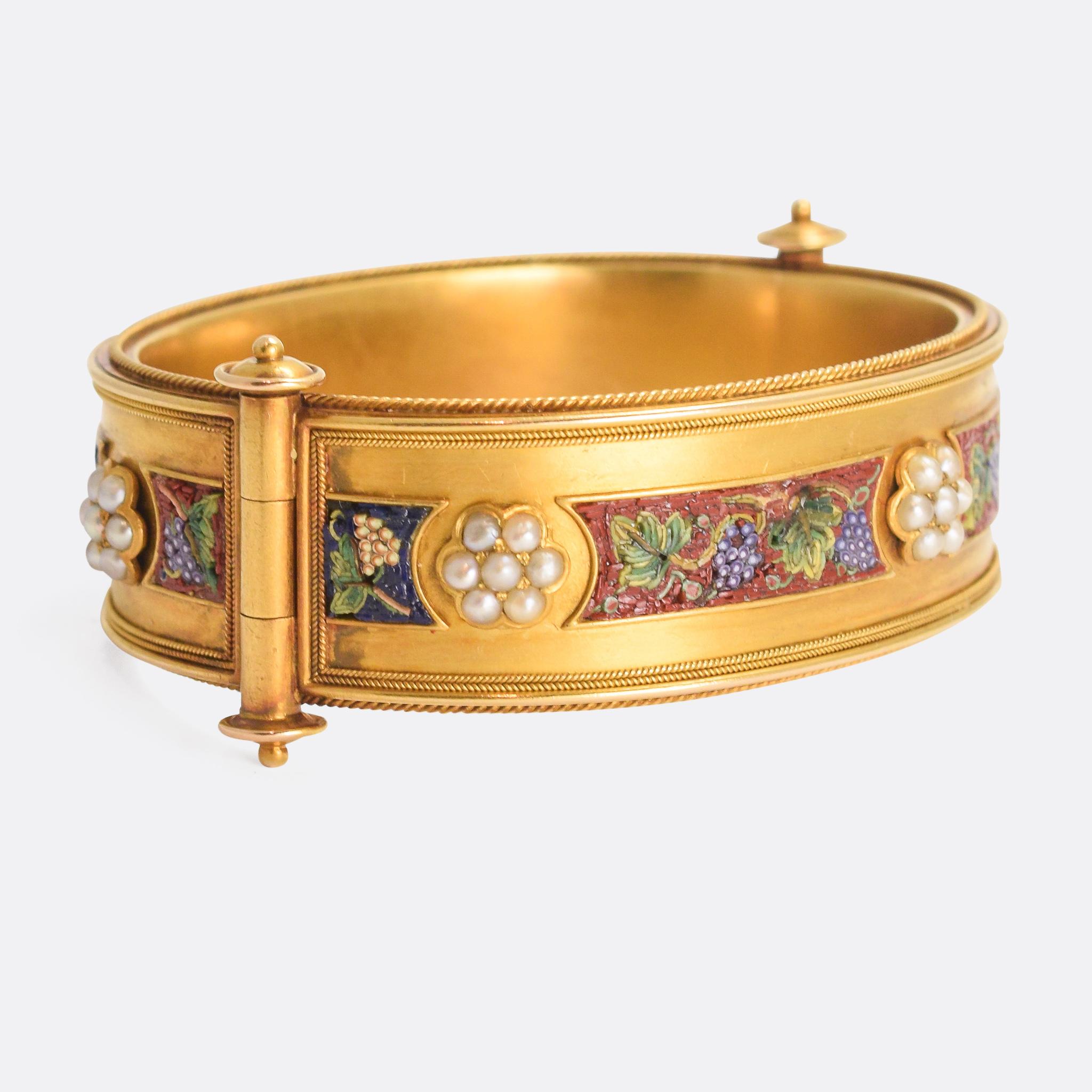 A spectacular mid-Victorian bangle set with eight micromosaic panels, as well as six natural pearl flower clusters. The micromosaics depict grape and vine motifs: red grapes on a blue background, and green grapes on a red background. It's modelled