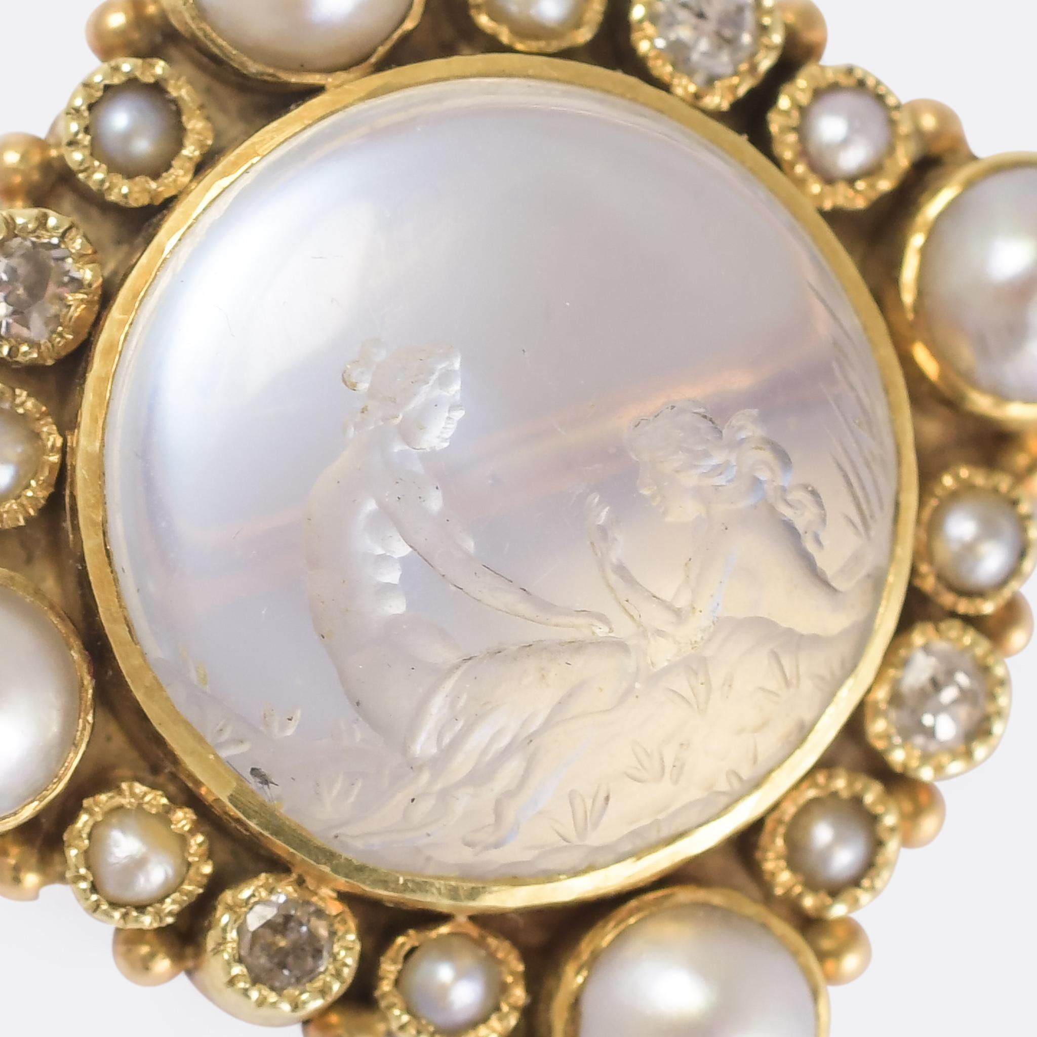 A beautiful Victorian brooch set with an intaglio carved moonstone centrepiece within a diamond and pearl set border. The scene depicted is of two classical women at a river bank, one bathing in the water, the other kneeling on the bank. The