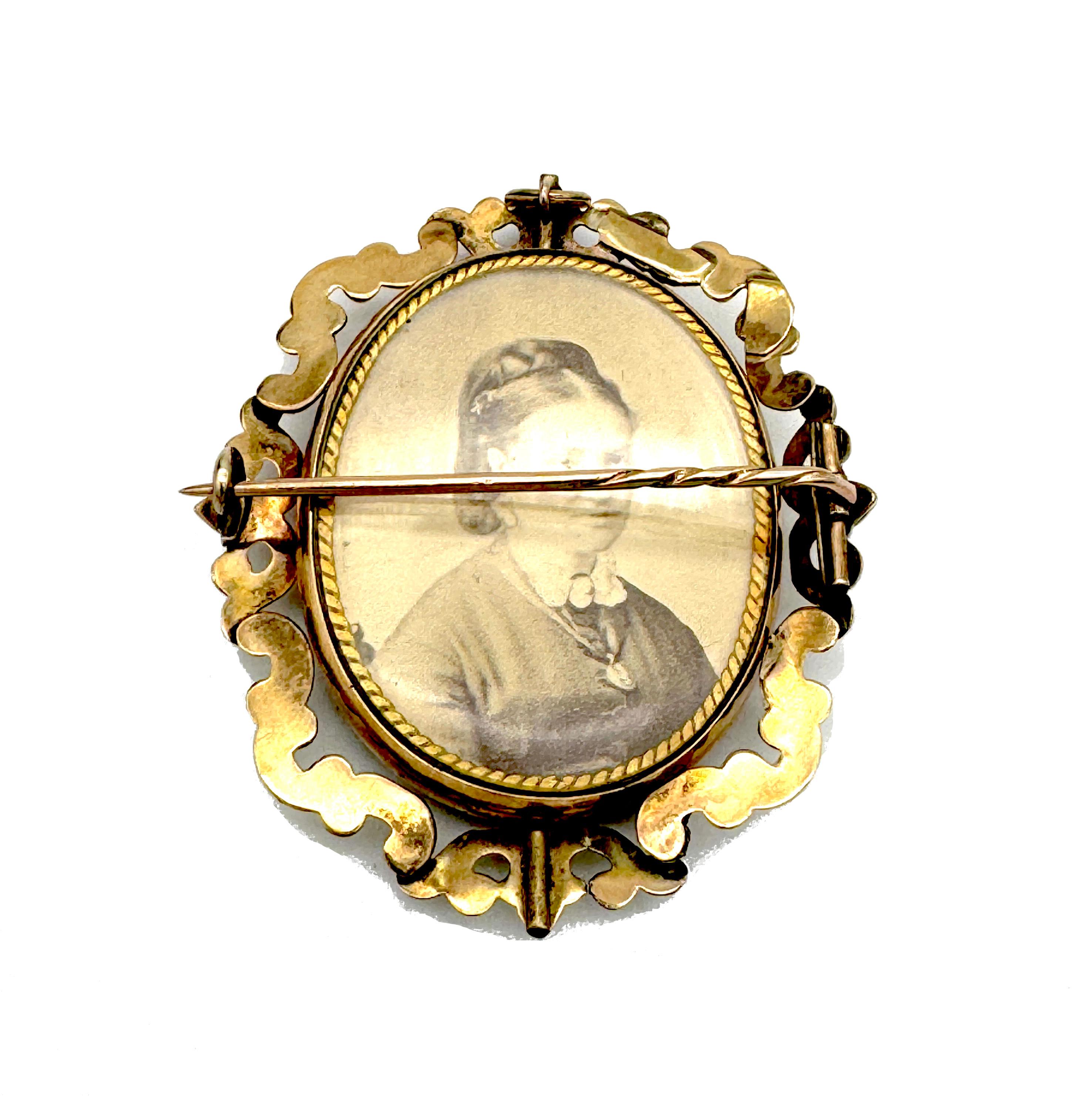 This mid 19th century Victorian mourning brooch is constructed as an outer frame with an inner revolving oval locket. The frame is designed as a succession of scrolls. At the top and at the bottom two revolving pins are securing the oval locket to