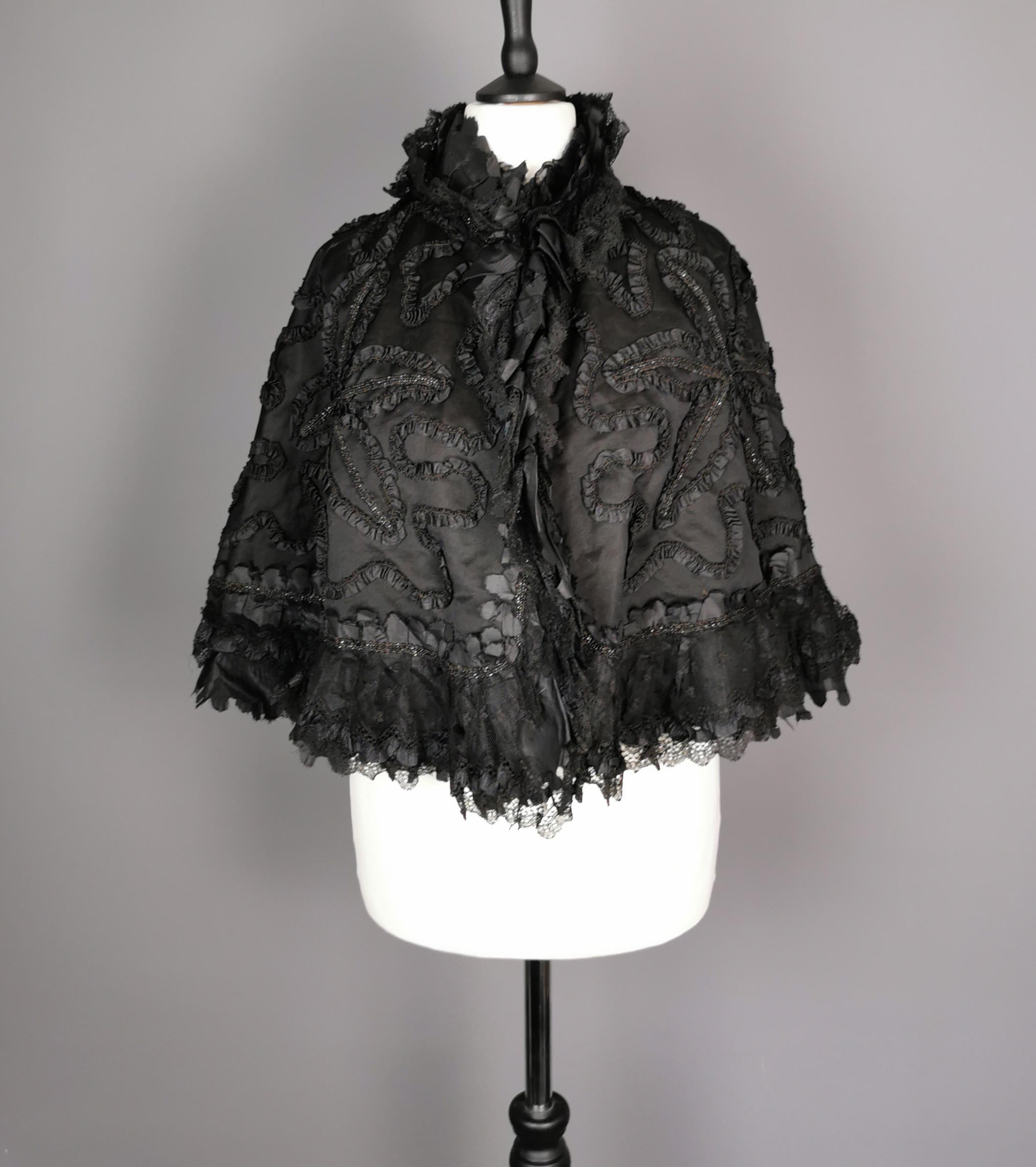 An absolutely beautiful Victorian mourning Cape with French jet beaded embellishments, and a silk swirl design trimmed in black lace.

The main outer of the cape is made in a black taffeta with a swirl design in black silk and the interior is lined