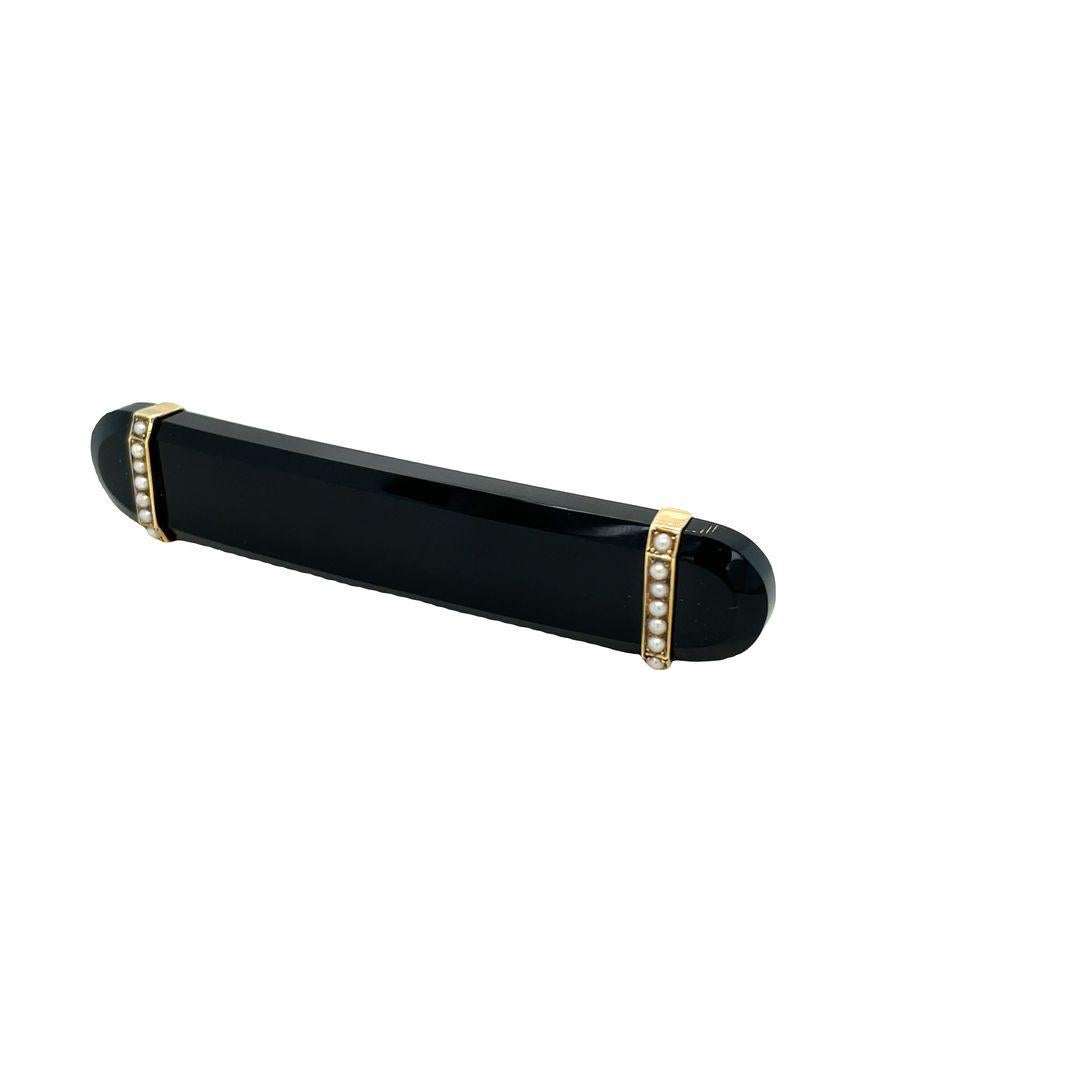 This is a beautiful Victorian brooch that combines modern minimalism with sentimental jewelry design. It features a glossy black onyx bar, measuring 2 2/3 inches in length, adorned with 14 small natural pearls set in rosy-yellow gold. The pearls are