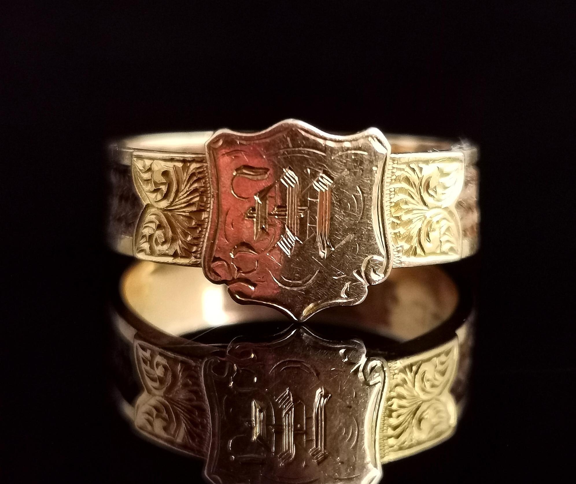 A handsome antique Victorian mourning ring.

Rich 18kt yellow gold with a central shield shaped cartouche with the letter M engraved in fancy script.

The gold band has finely woven brown hair running through the centre with engraved gold sections