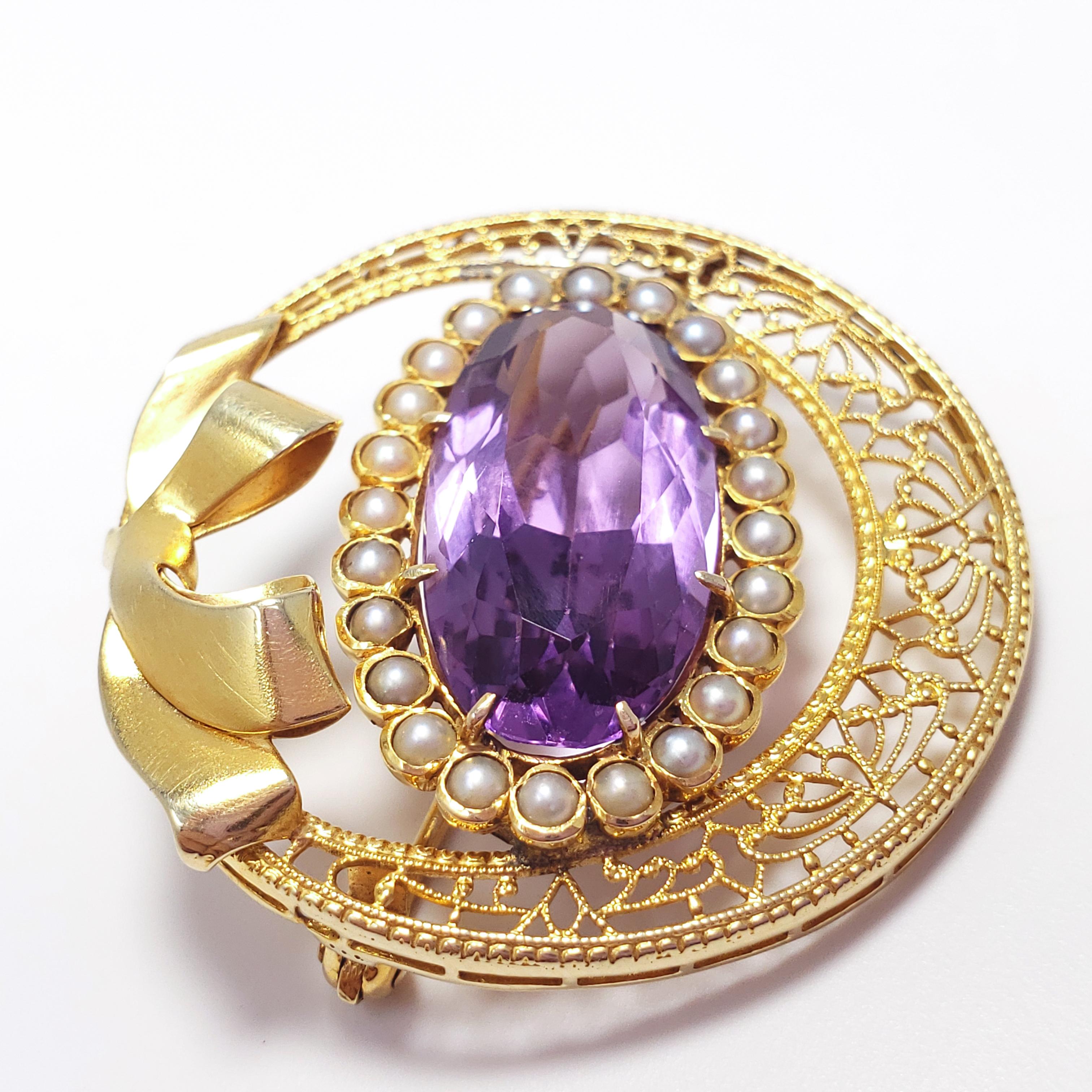 A dainty Victorian brooch for the most elegant woman! A single prong-set faceted amethyst is surrounded by natural seeded pearls in round bezels. All set in a 14KT gold round filigree setting, accented with a bow motif. Made c. early 1900s. This