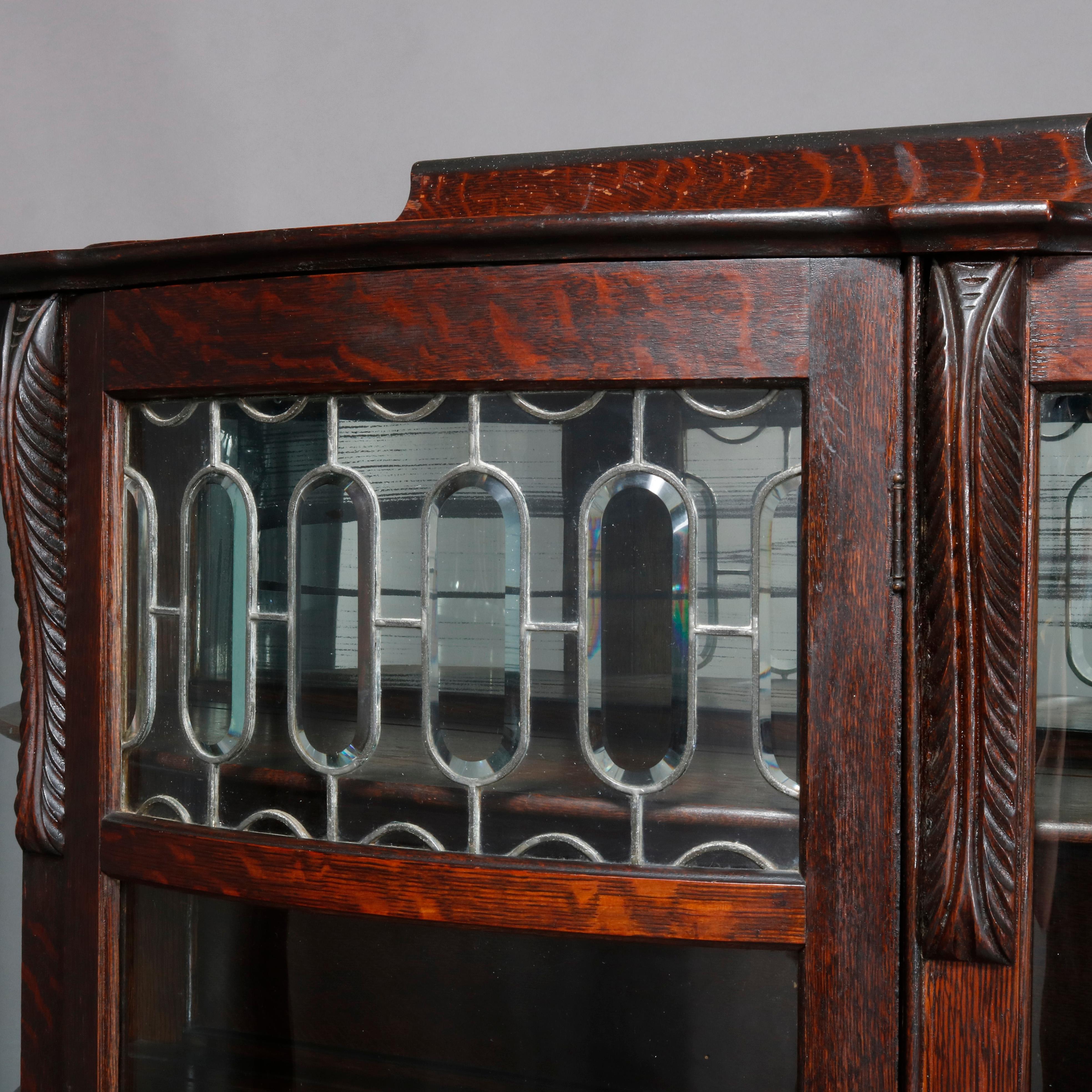An antique Victorian china cabinet offers quarter sawn oak construction with shaped backsplash surmounting case with stylized acanthus capitals flanking single curved glass door with leaded glass panel, opening to mirrored and shelved interior,