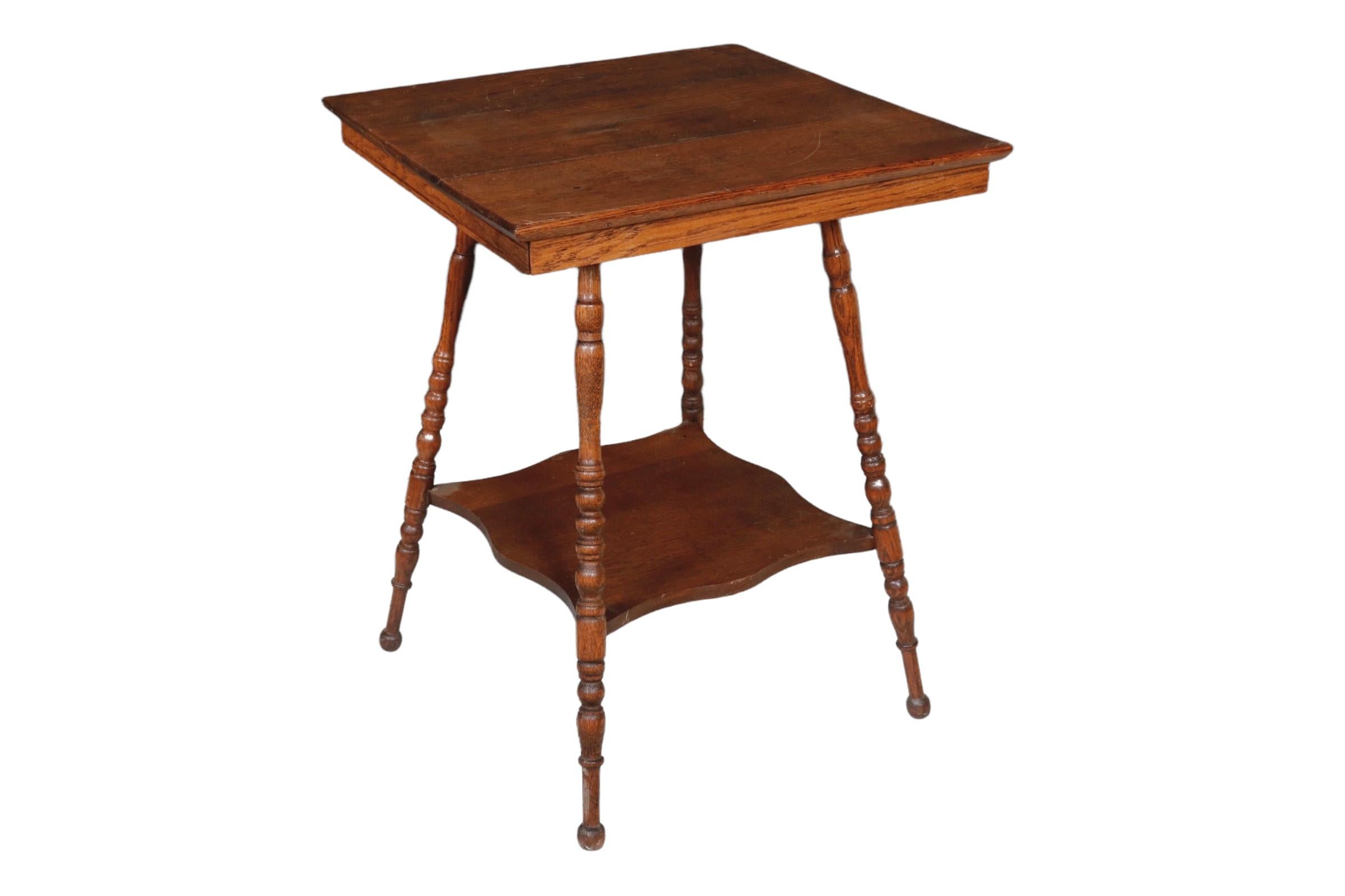 An antique oak parlor table with turned legs from the Victorian period. USA, circa early 20th century.

Features a lower shelf and carved apron.

Dimensions: 24” L x 24” W x 30” H.
 