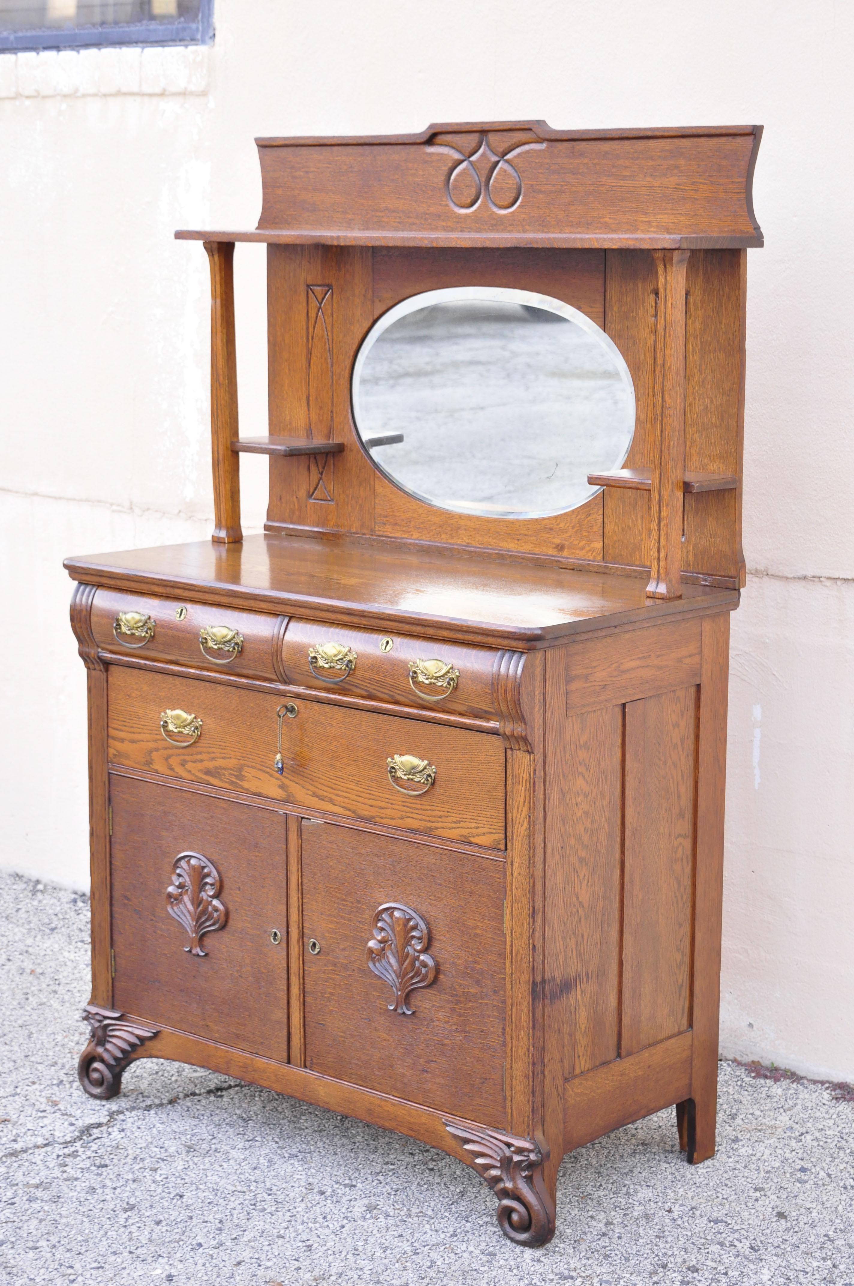 Antique Victorian oak wood sideboard buffett with Mirror Hutch Backsplash Shelf. Item features oval beveled mirror backsplash shelf, carved winged griffin feet, brass hardware, beautiful wood grain, nicely carved details, 3 dovetailed drawers, 2