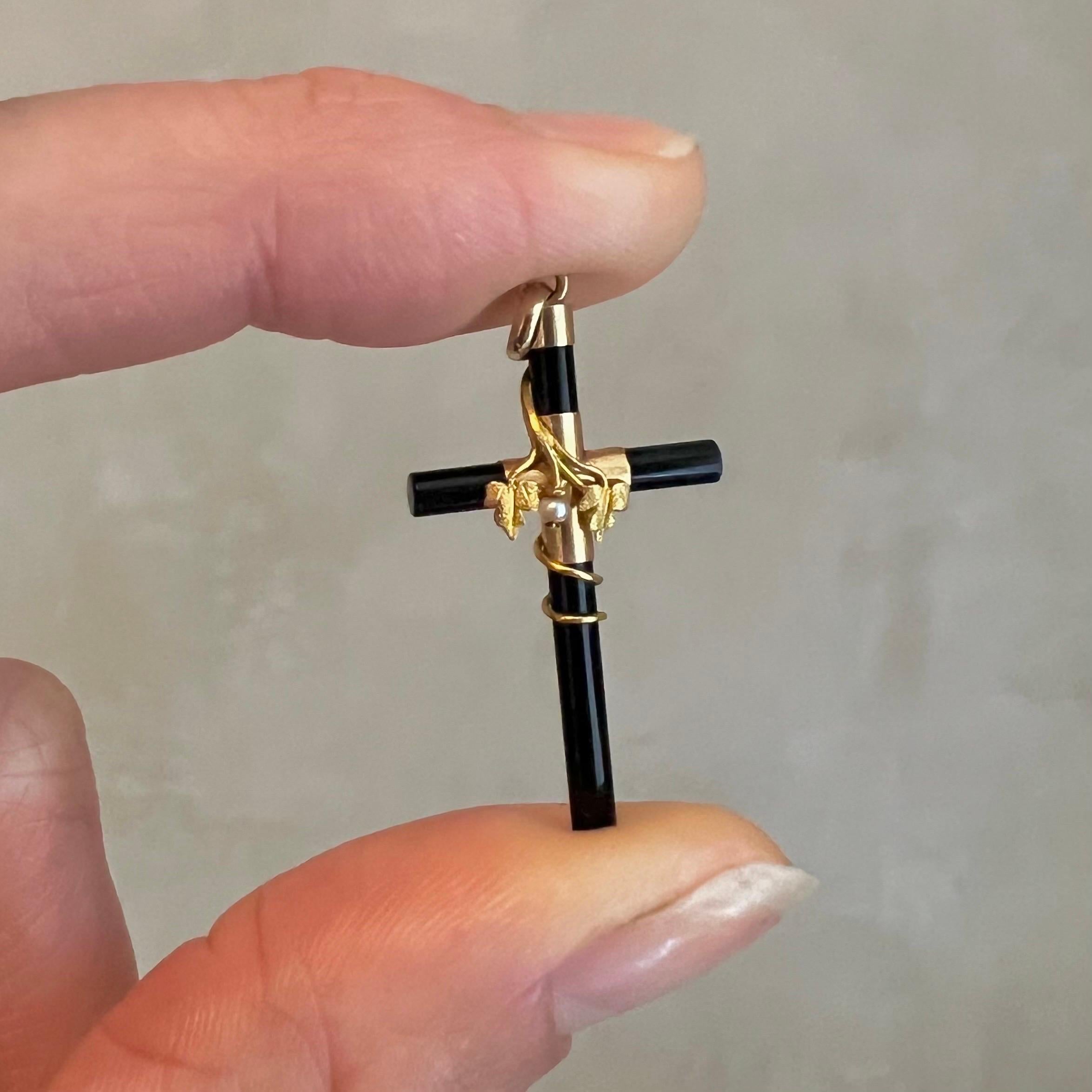 A Victorian onyx cross pendant set with a single seed pearl and adorned with a 14 karat gold floral design. This pendant is a captivating embodiment of the elegance and symbolism of the Victorian era. Crafted during the 19th century, this pendant