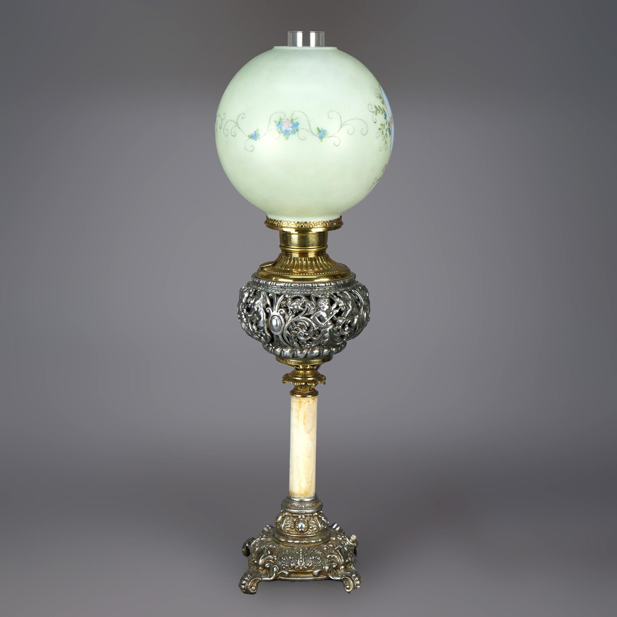 Une lampe de salon victorienne antique offre un abat-jour en verre avec une réserve de chérubins et des éléments floraux peints à la main, sur une base avec une fontaine argentée et dorée percée de putti et de dragon, reposant sur une seule colonne
