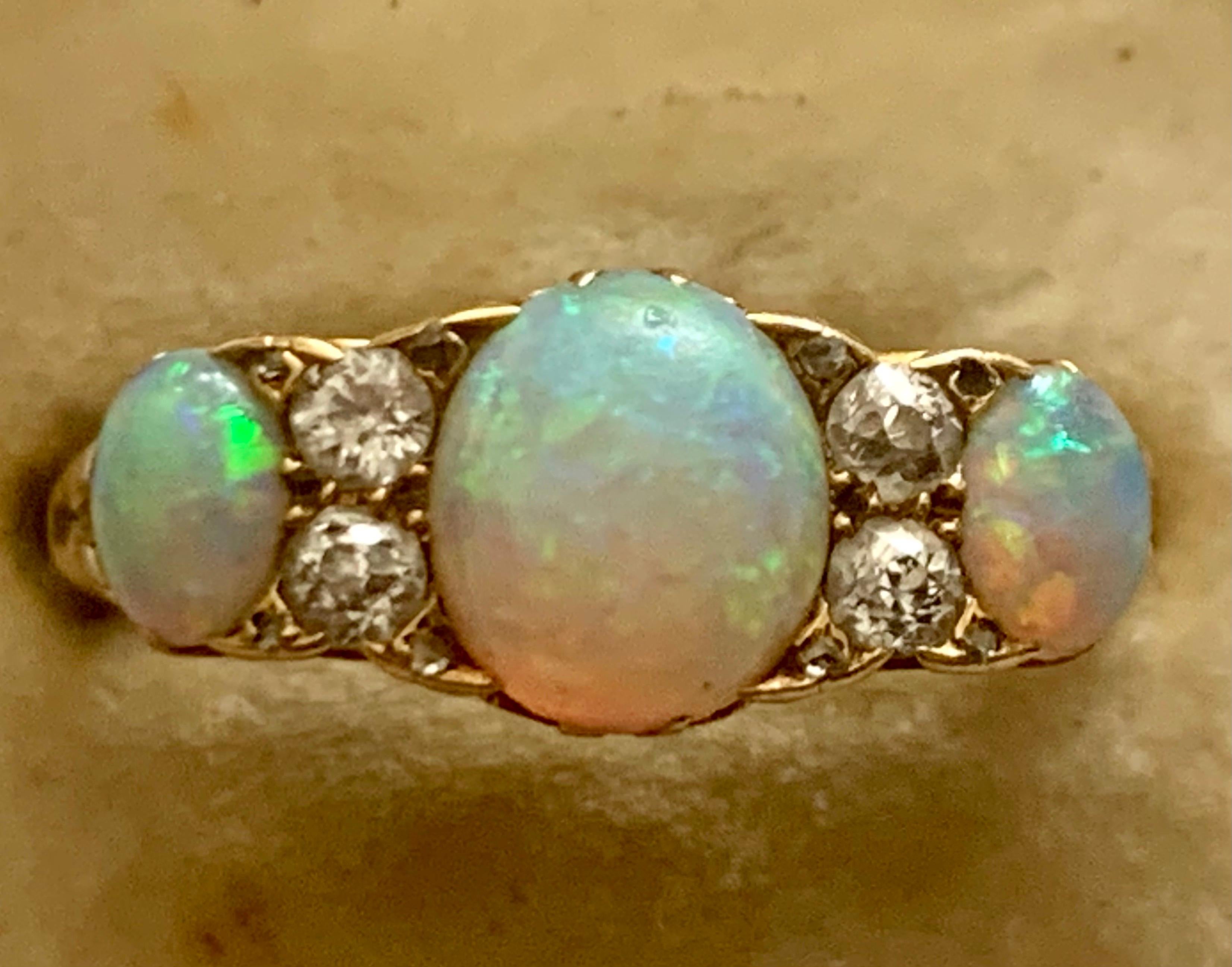 A beautiful Antique late Victorian cluster ring adorned with a trilogy of colourful natural Opals with 4 Old European cut Diamonds set in between. The Opals are a rainbow of colours shimmering and changing with the light. They radiate all different