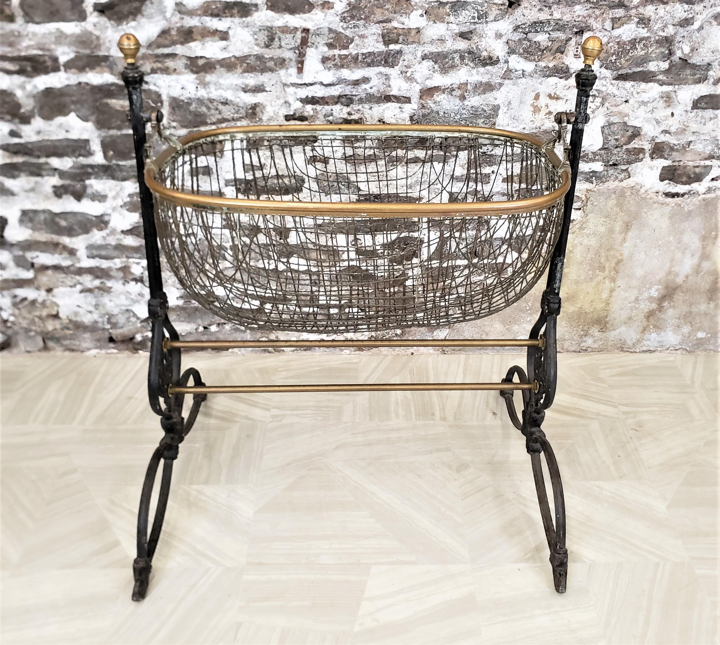 This antique baby cradle is unsigned, but presumed to have originated from England and date to approximately 1880 and done in the period Victorian style. The frame or stand for the cradle is composed of cast iron with brass accents on the finials