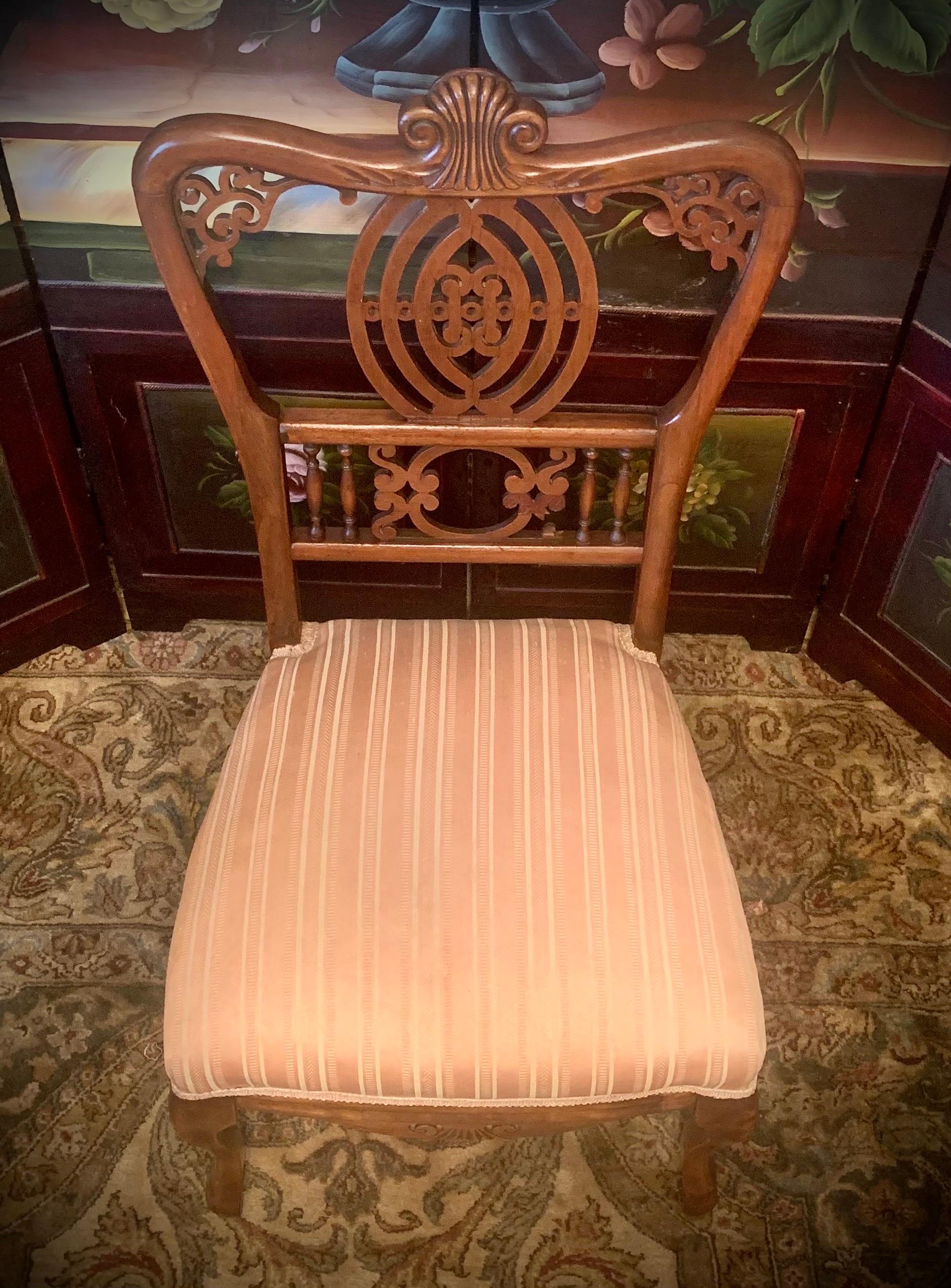 Circa 1890-1910 this antique Victorian slipper chair is American made and constructed of solid, smooth mahogany with ornately carved wood plane detail, lathe-fashioned spindles, cabriole legs, and a lowered seat.  The blush pink and cream striped