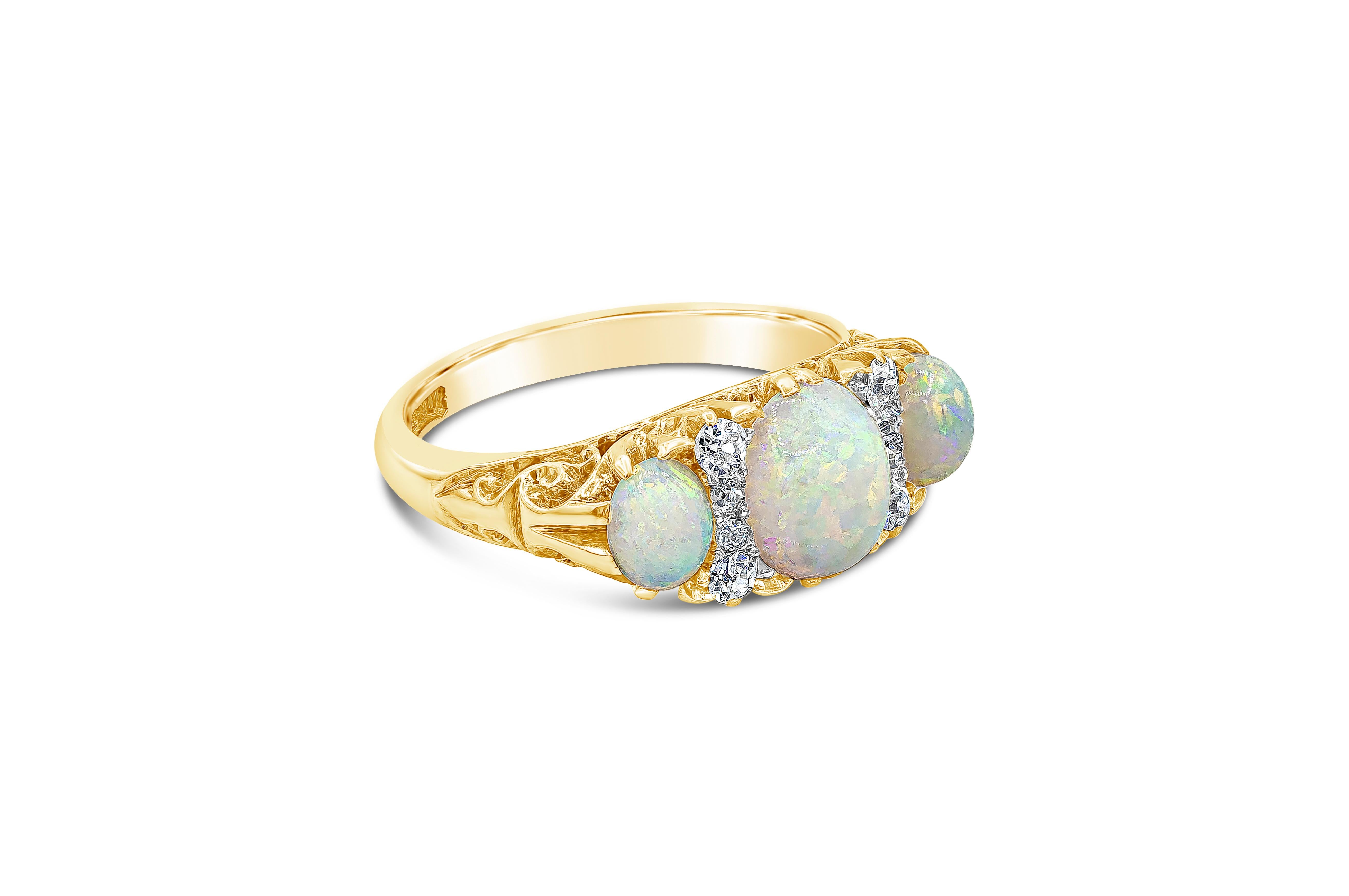 An antique three-stone ring from the Victorian era showcasing three beautiful oval opals spaced by a row of old mine diamonds. Diamonds set in 18k yellow gold finished with hand-carved design. Opal weighs approximately 2.00 carats total; diamonds